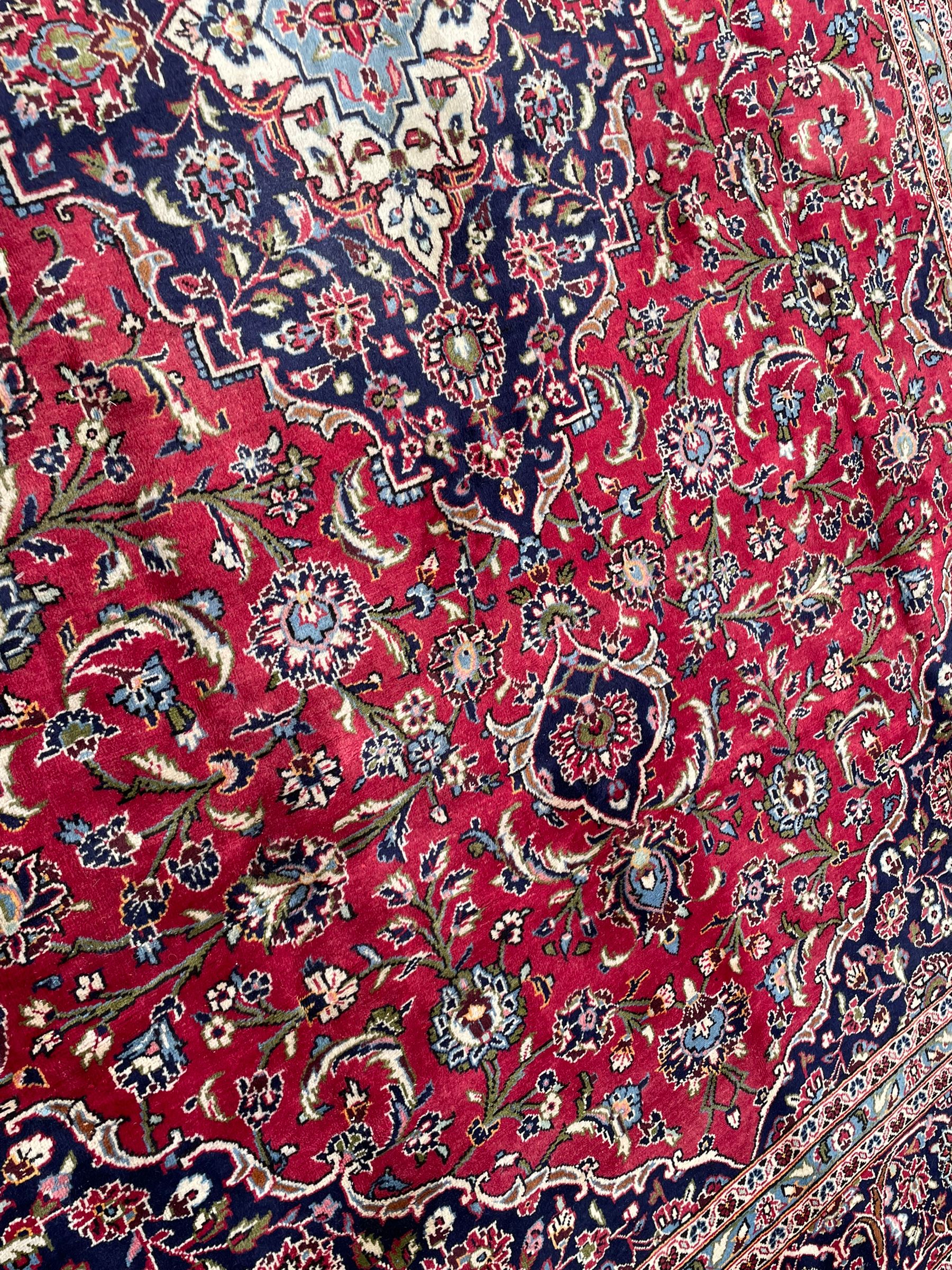 Central Persian Kashan crimson ground carpet, central  floral pole medallion with matching spandrels within a field of scrolling palmette motifs and foliage, the heavily banded indigo border with repeating plant motifs interlaced with scrolled branches