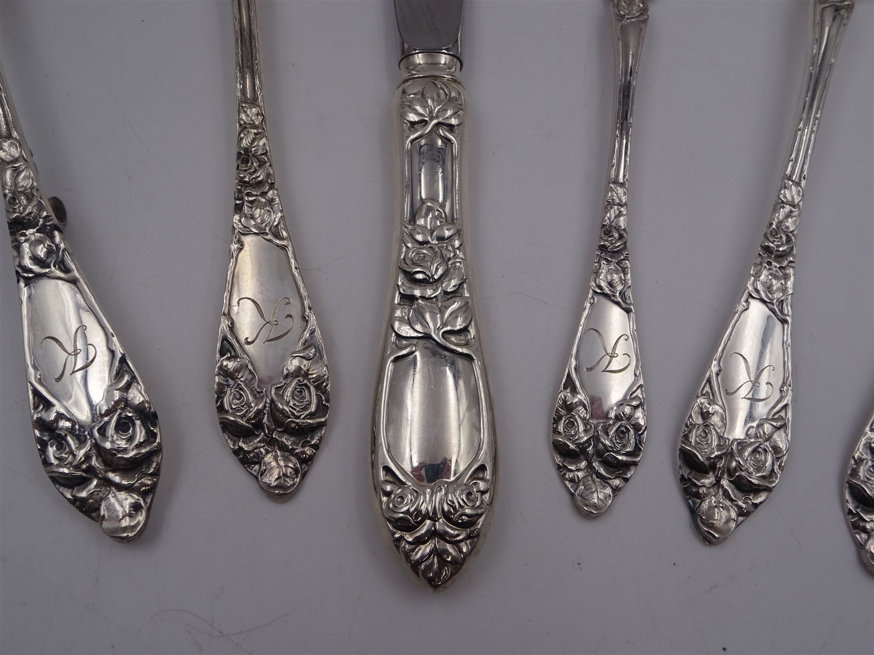 1930s Norwegian silver cutlery for six place settings, comprising table spoons, table forks and silver handled table knives, cake forks, tea spoons and demitasse spoons, one cake slice, serving spoon, sauce ladle and a pair of silver handled servers, all embossed with rose decoration and engraved with initial K to terminal and 10/9 1932 verso, stamped NM 830s