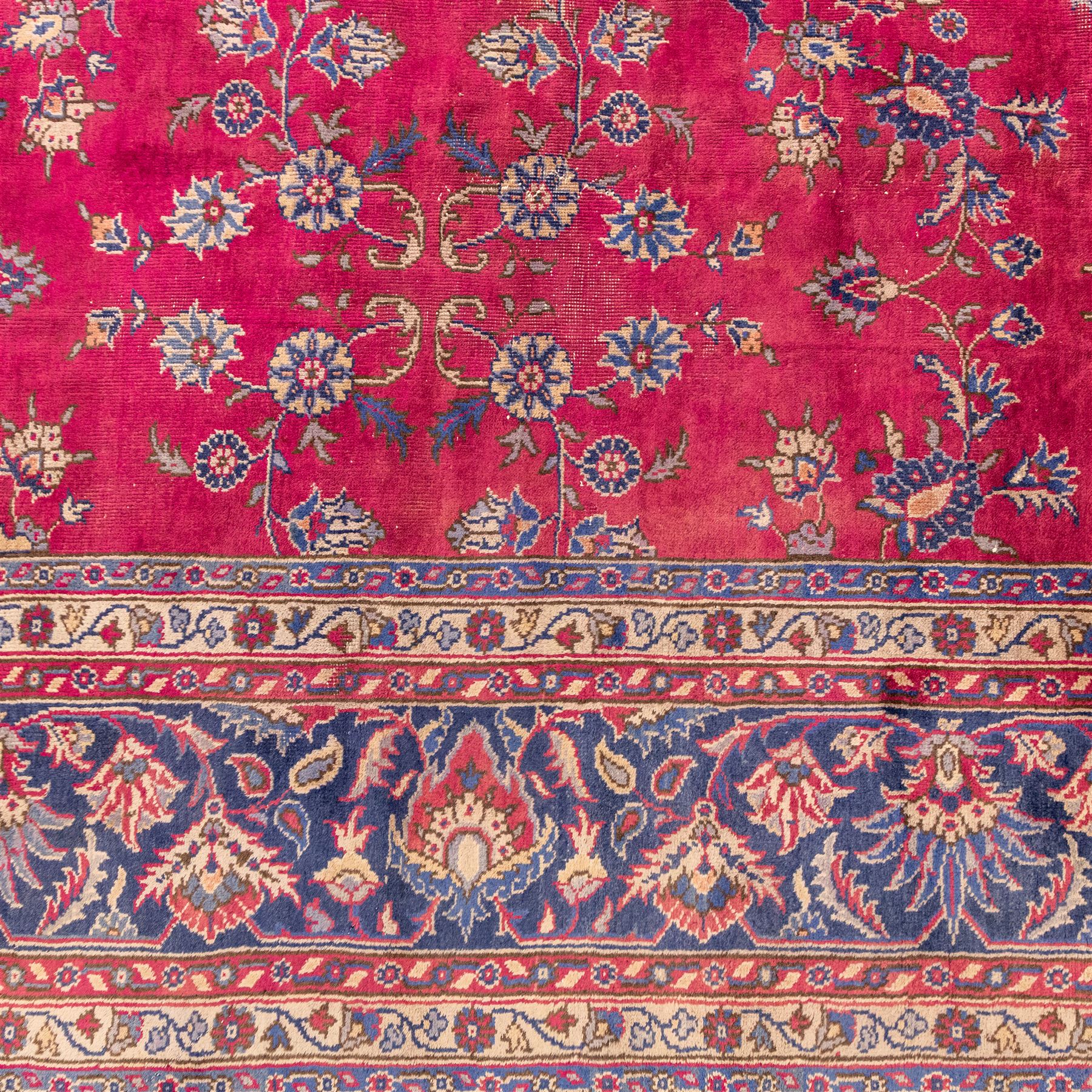Large Persian-style mahal-type hand-knotted carpet, of rectangular form with a deep crimson field decorated with an all-over arrangement of stylized floral sprays and palmettes, with a central subtle medallion composition enclosed by a dark navy main border of scrolling floral motifs between narrow guard stripes with fringe ends 