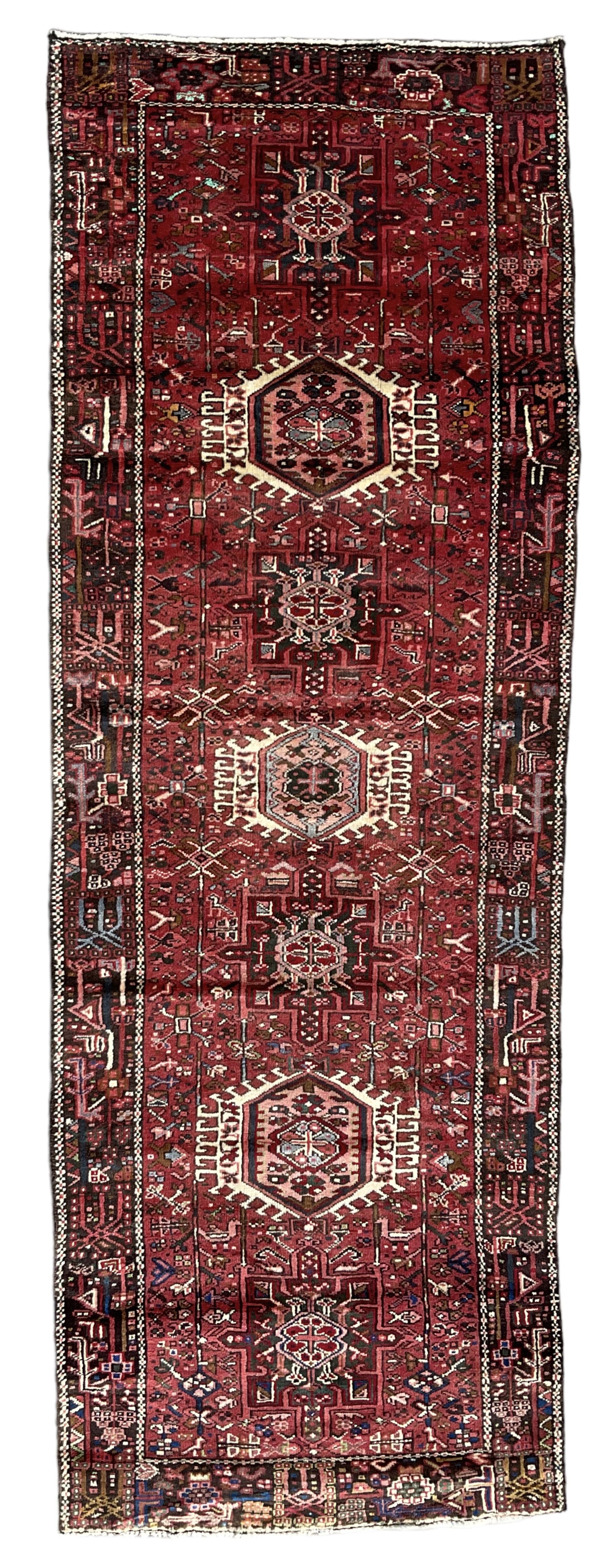 Persian Karajeh crimson ground runner rug, the field set with seven geometric lozenge medallions, the field decorated all over with stylised plant motifs, the banded border with repeating geometric shapes and patterns