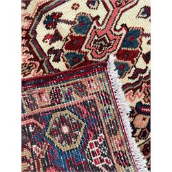 Persian Heriz red ground rug, central scrolled medallion on dark ground decorated with floral motifs, the surrounding field decorated with stylised plant motifs and smaller geometric symbols, guarded border with repeating pattern punctuated with rosettes and flower heads 