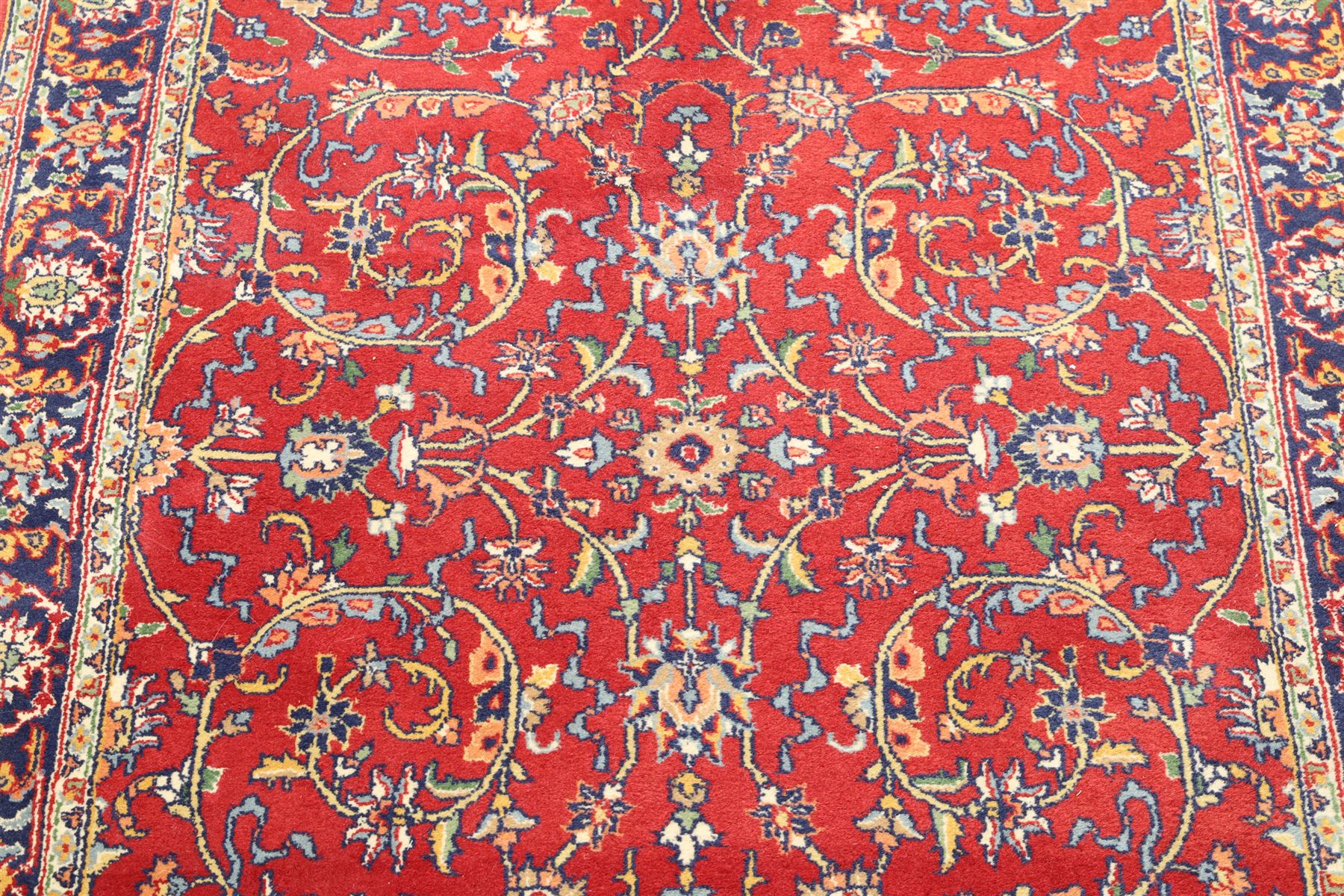 Persian Kashan crimson ground rug decorated with scrolling foliage, the indigo guard stripes with repeating stylised palmette motifs