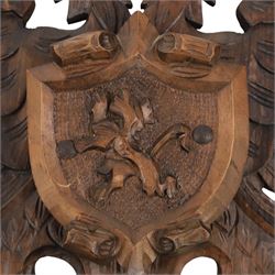 Carved wooden wall plaque, decorated with foliate scrolls, with two reproduction swords attached, together with five other wooden plaques with foliate scrolls and shields