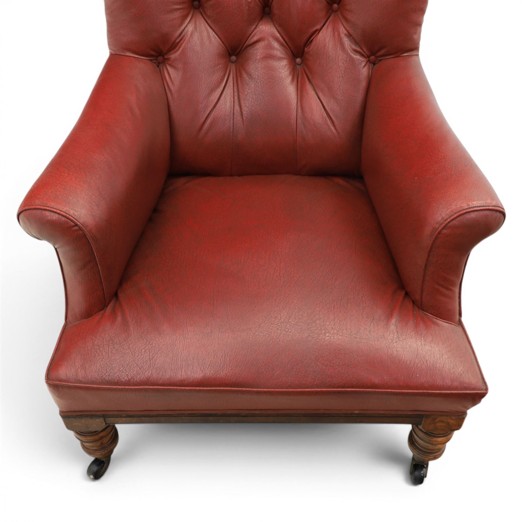 Early 20th century style oxblood red leather Chesterfield armchair, deep buttoned shaped back over padded scroll arms and loose seat cushion, raised on turned mahogany front supports with brass caps and castors