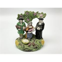 Two early 19th century Staffordshire figure 'Tithe Pig' groups, modelled as parson, farmer, wife and infant before bocage support, upon a moulded base detailed with piglets, wheat sheaves and baskets of eggs, each approximately H14.5cm