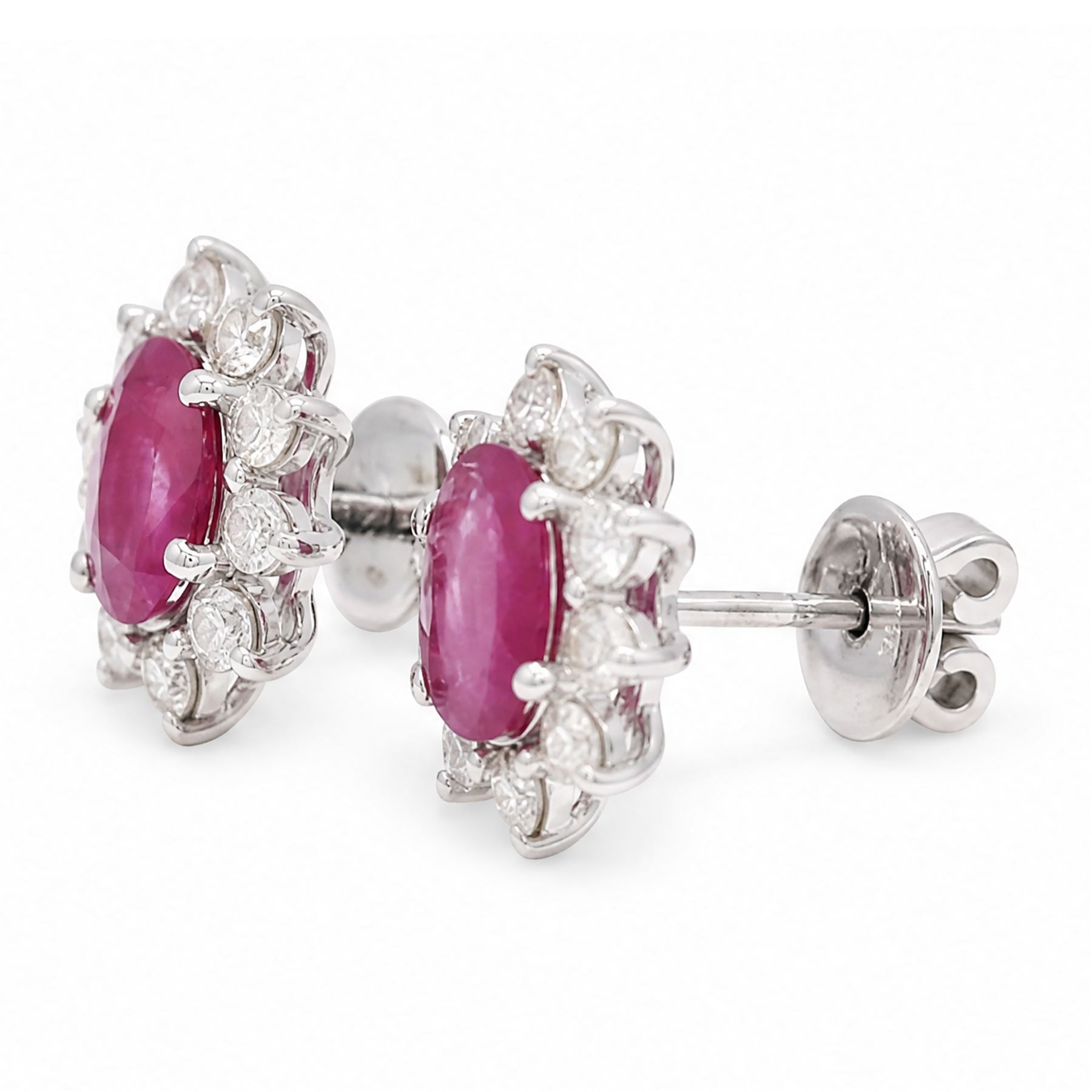 Pair of 18ct white gold ruby and diamond earrings, each stud set with a single oval cut ruby and surrounded by ten round brilliant cut diamonds, stamped, total ruby weight approx 1.40 carat, total diamond weight approx 0.60 carat
