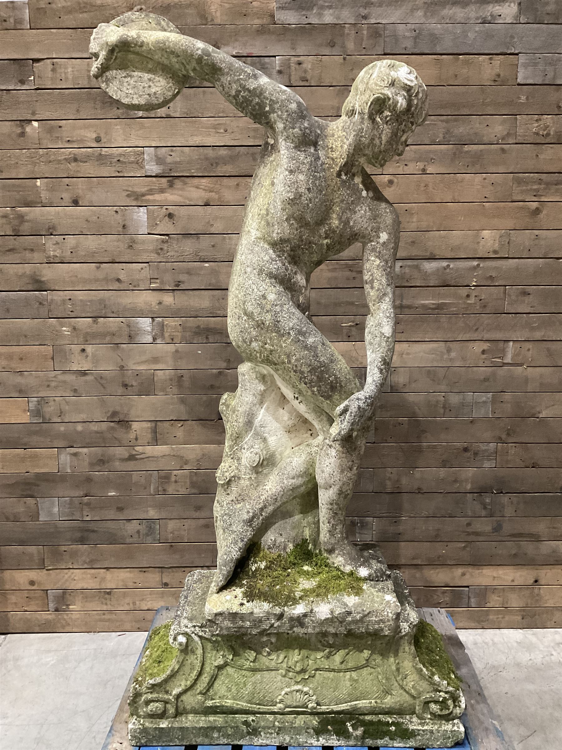 Life-size weathered cast stone Greek Discus Athlete, seated on rectangular slab raised on associated architectural plinth