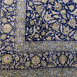 Central Persian Kashan hand-knotted rug, deep blue all-over field, finely decorated with dense scrolling floral sprays, palmettes, and flowering vines in ivory, soft gold, and pale green tones, enclosed by a multi-band floral border with corresponding guard stripes, with cotton fringe ends, signed Shah Abassi Workshop 