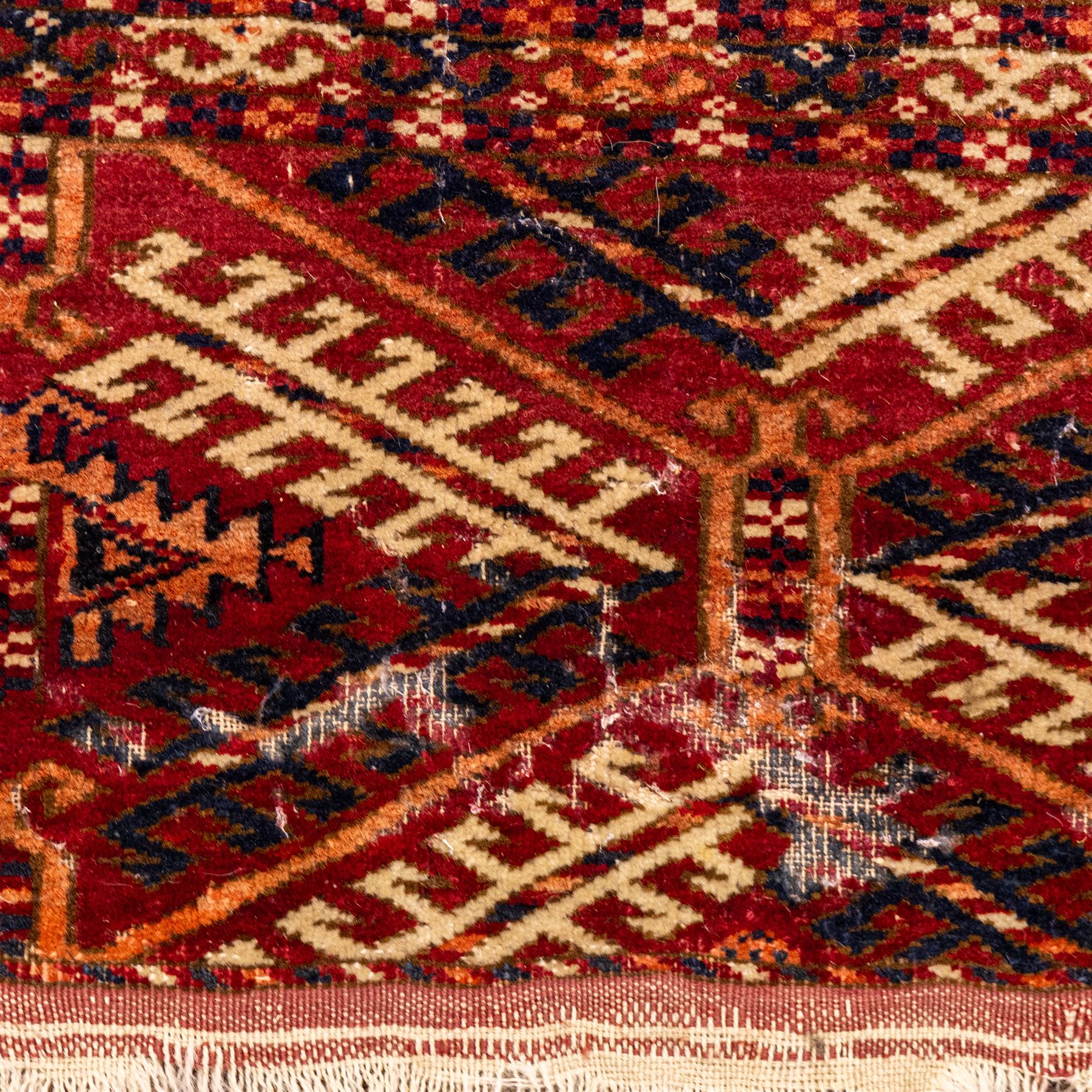 Vintage Bokhara hand-knotted rug, madder field woven in rows of octagonal Tekke guls arranged in vertical columns, each enclosing angular cruciform devices and tribal motifs, divided by narrow indigo lines, within multiple geometric borders incorporating stepped lozenges and latch hook devices, with cotton fringe ends 
