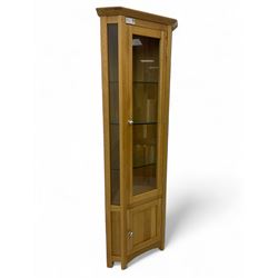 Contemporary light oak corner display cabinet, projecting cornice over single glazed door enclosing three glass shelves, the base fitted with panelled cupboard enclosing single oak shelf, on stile supports