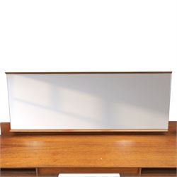 Austinsuite - mid 20th century teak headboard with bedside cabinets and matching  mirrored dressing table, the headboard with floating single drawer bedsides raised on a single tapering support, the dressing table with attached tilting mirror, above rectangular top with kneehole and two banks of two drawers, raised on tapering supports

Headboard H 84cm, D 40cm, W 229cm, W between bedsides 151cm 
Dressing table H 113cm D 44cm, W 149cm, H to underside of dresser 61cm