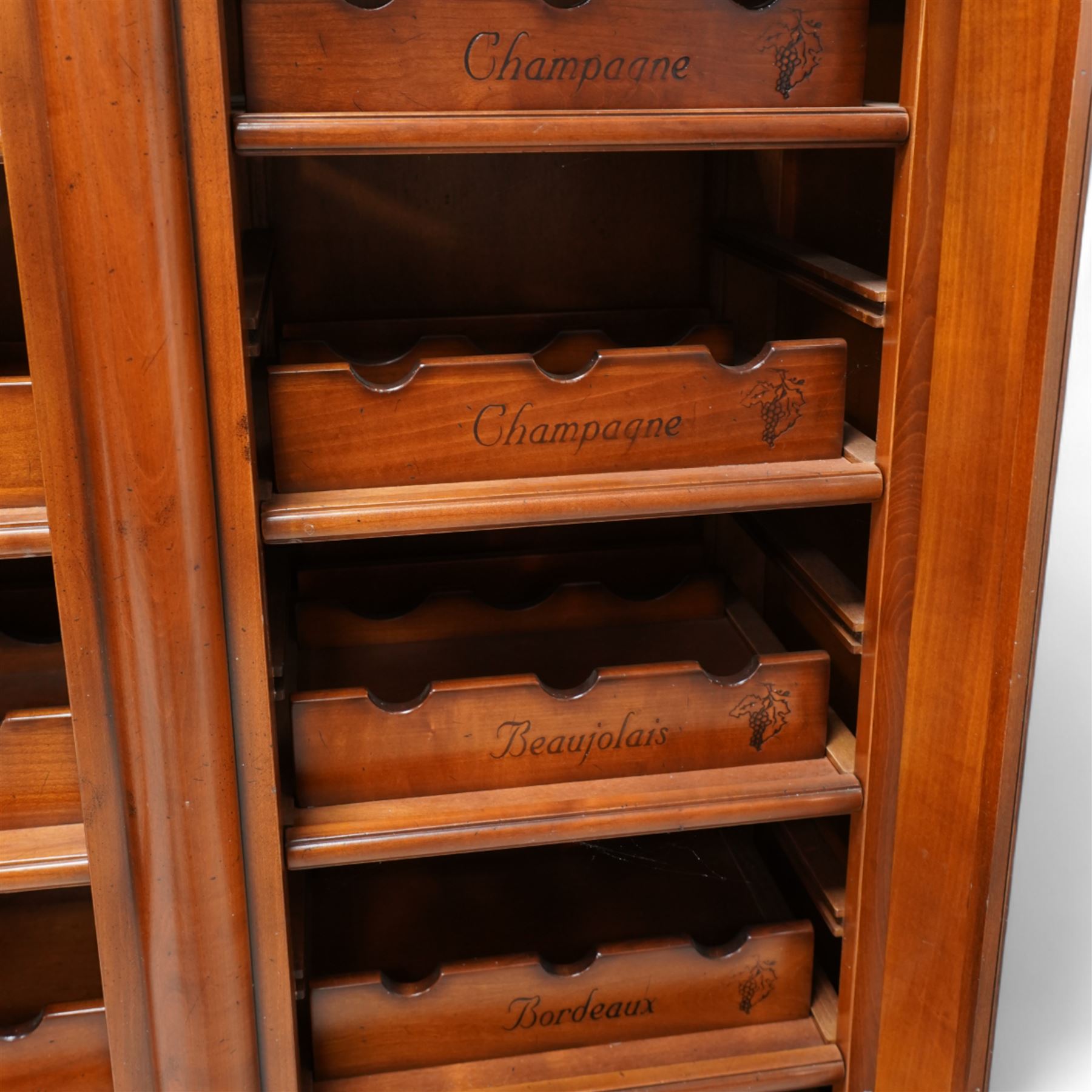 Cherrywood wine rack cabinet, moulded rectangular top over two glazed doors, fitted with eight slides each with three bottle holders inscribed with various wine types, single long drawer to the base 