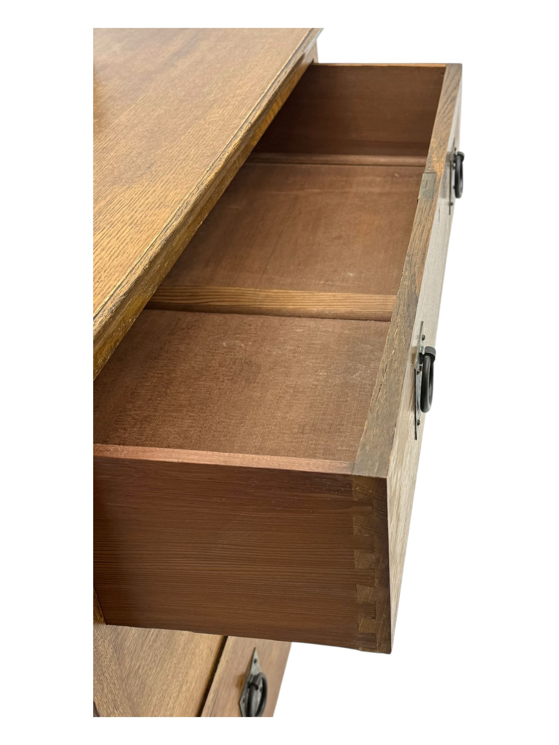 Early 20th century Arts and Crafts oak dressing chest, the arched mirror flanked by floral marquetry inlaid uprights above a shelf and drawer, over three long drawers with square hammered metal plates and circular pulls, on slender supports with castors