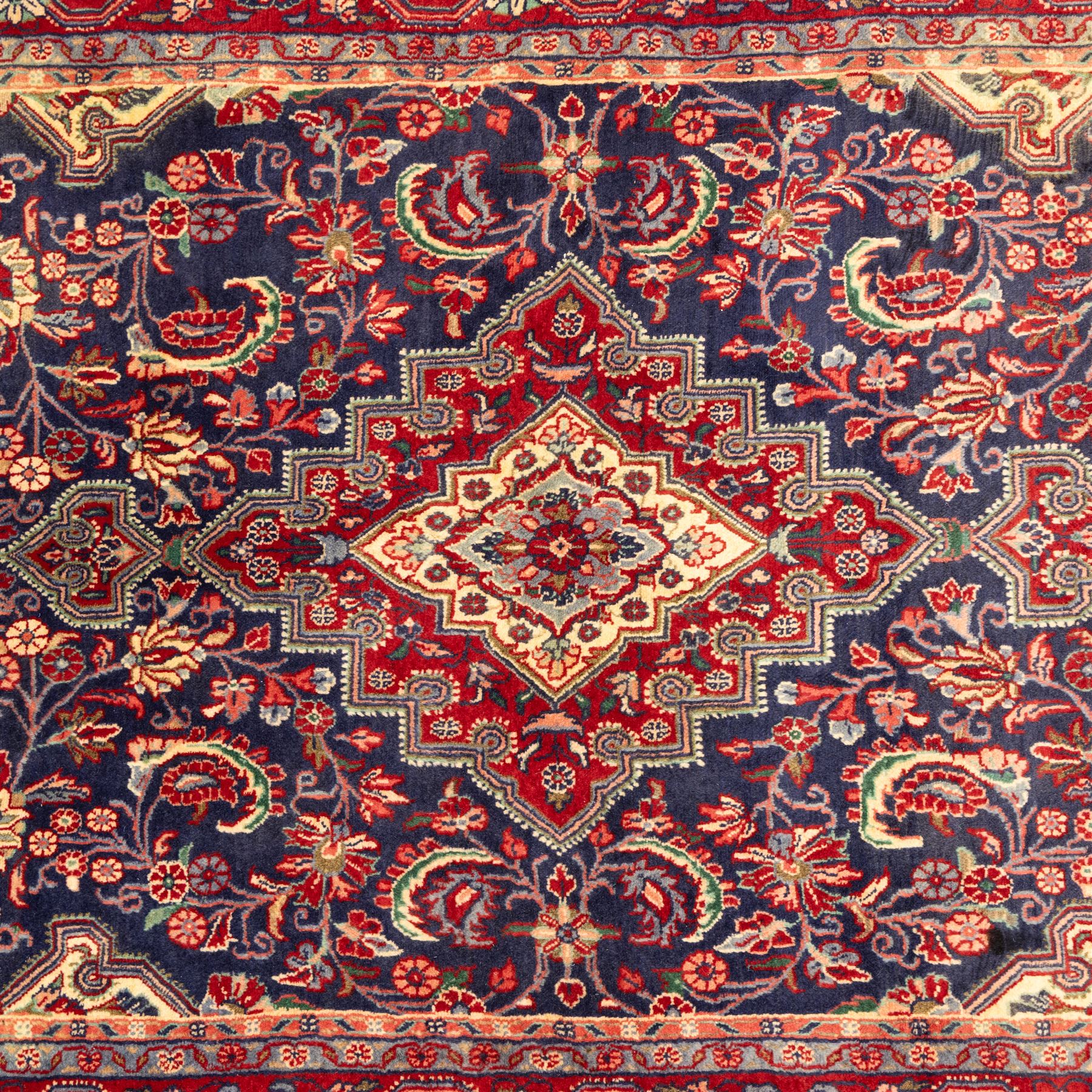 North West Persian hand-knotted Sarouk rug, central navy ground field with cusped lozenge medallion with pendant motifs, scrolling palmettes, and floral sprays, cream spandrels, and madder red border of stylized rosettes and leafy meandering vines between multiple guard stripes 