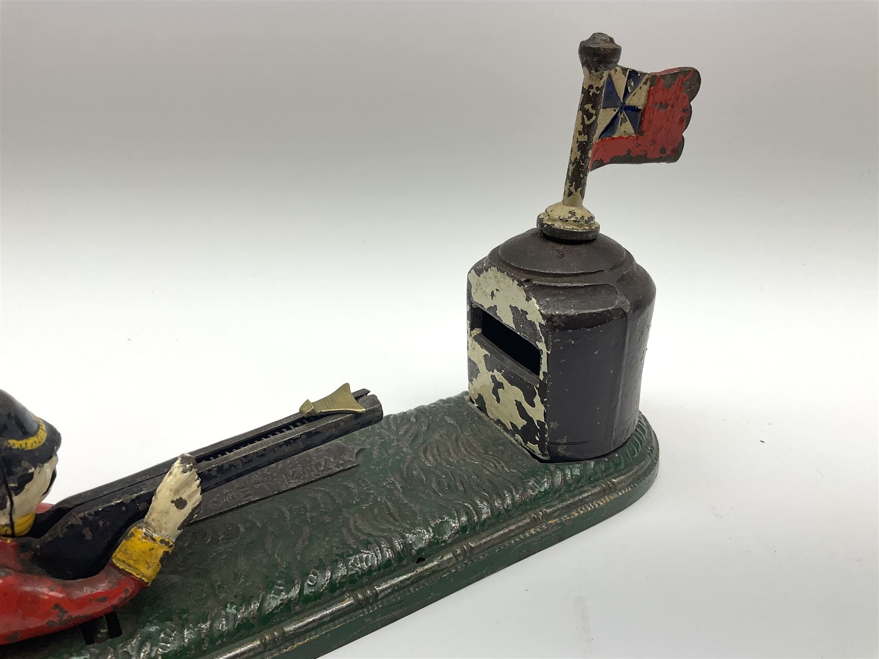 Very rare 19th century John Harper & Co. mechanical cast-iron money box, registered number 33821 patented 1885, inscribed on metal plaque 'Wimbledon Bank', based on the Queen's Trophy for shooting at Wimbledon, depicting a British Infantry man in red tunic and blue trousers lying on the ground using a gun to fire a brass coin launcher into a pill box with removable moving flag above L30cm