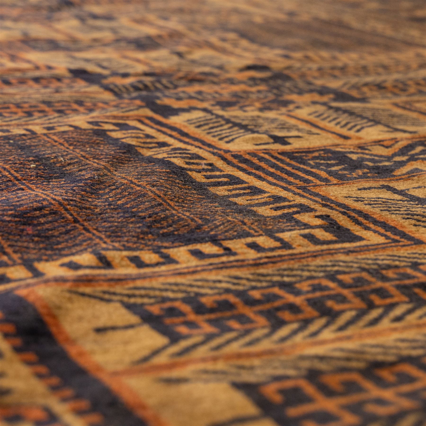 Baluch tribal style rug, dark indigo field with rows of linked gul and angular medallions in madder, camel, and ivory tones, within multiple geometric borders, including the main border of stylised animals