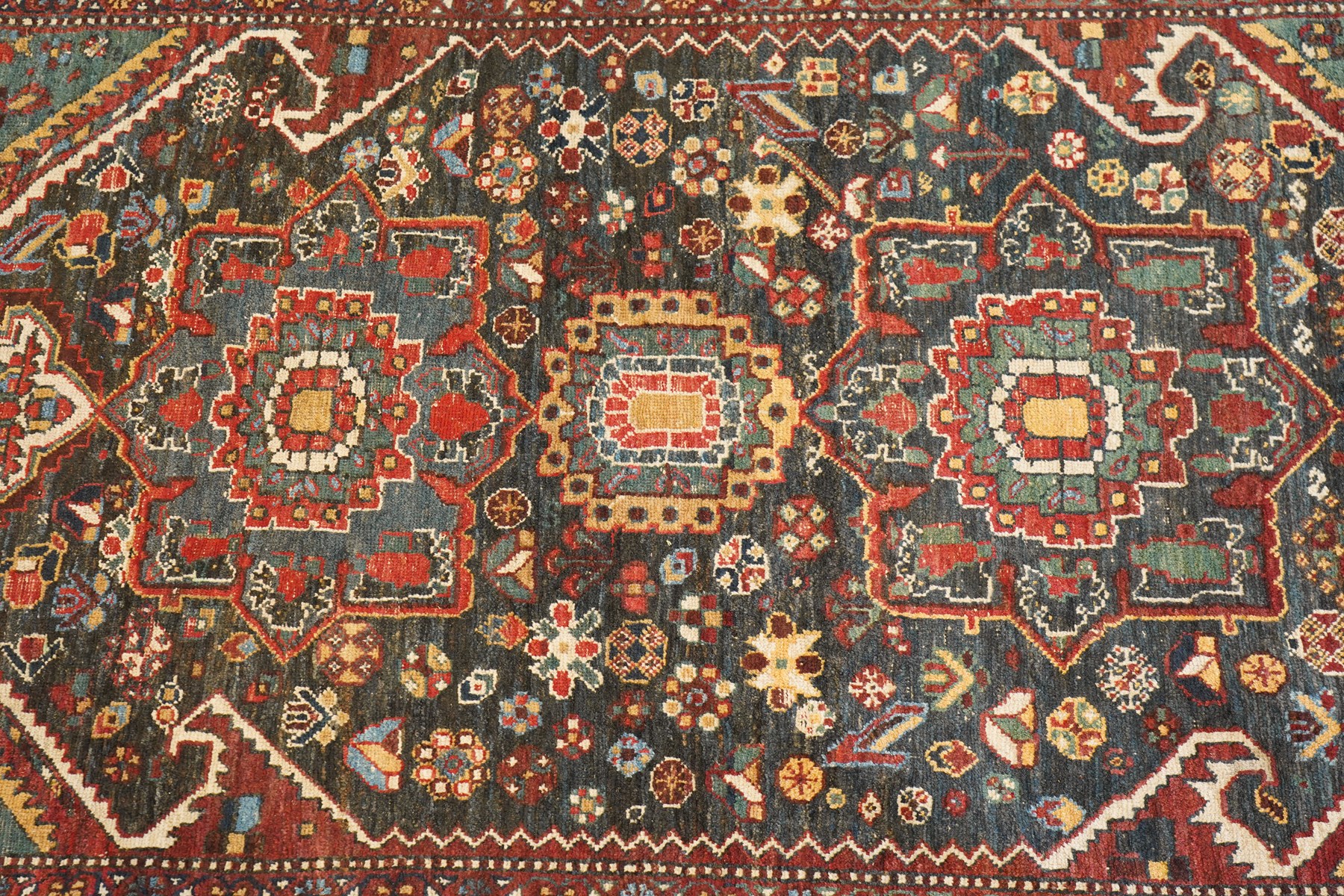 Antique Persian Qashqai dark indigo ground tribal rug, the busy field decorated with a geometric triple pole medallion surrounded by numerous stylised plant motifs with contrasting cyan spandrels, the multiple guard bands woven with stylised palmettes and foliage