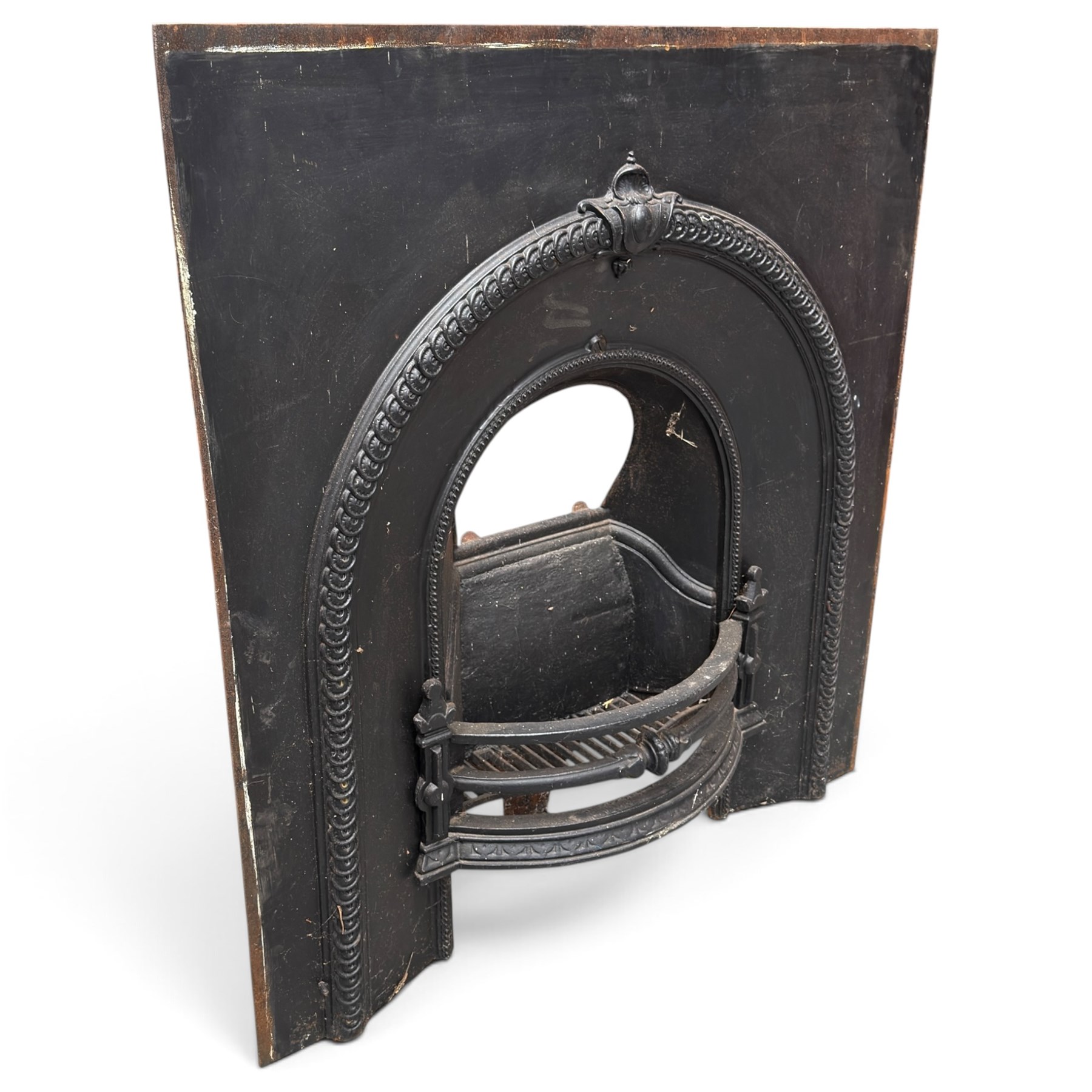Late Victorian black-painted cast iron fireplace, the arched surround with anthemion cartouche and guilloche-moulded border, enclosing a bow-front fire basket with finialled standards, railed front and leaf-cast apron, with sheet-metal backplate