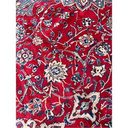 Kashan crimson ground carpet, overall floral design, the central medallion surrounded by trailing leafy branches and palmettes, scrolling border decorated with stylised plant motifs, within guard stripes
