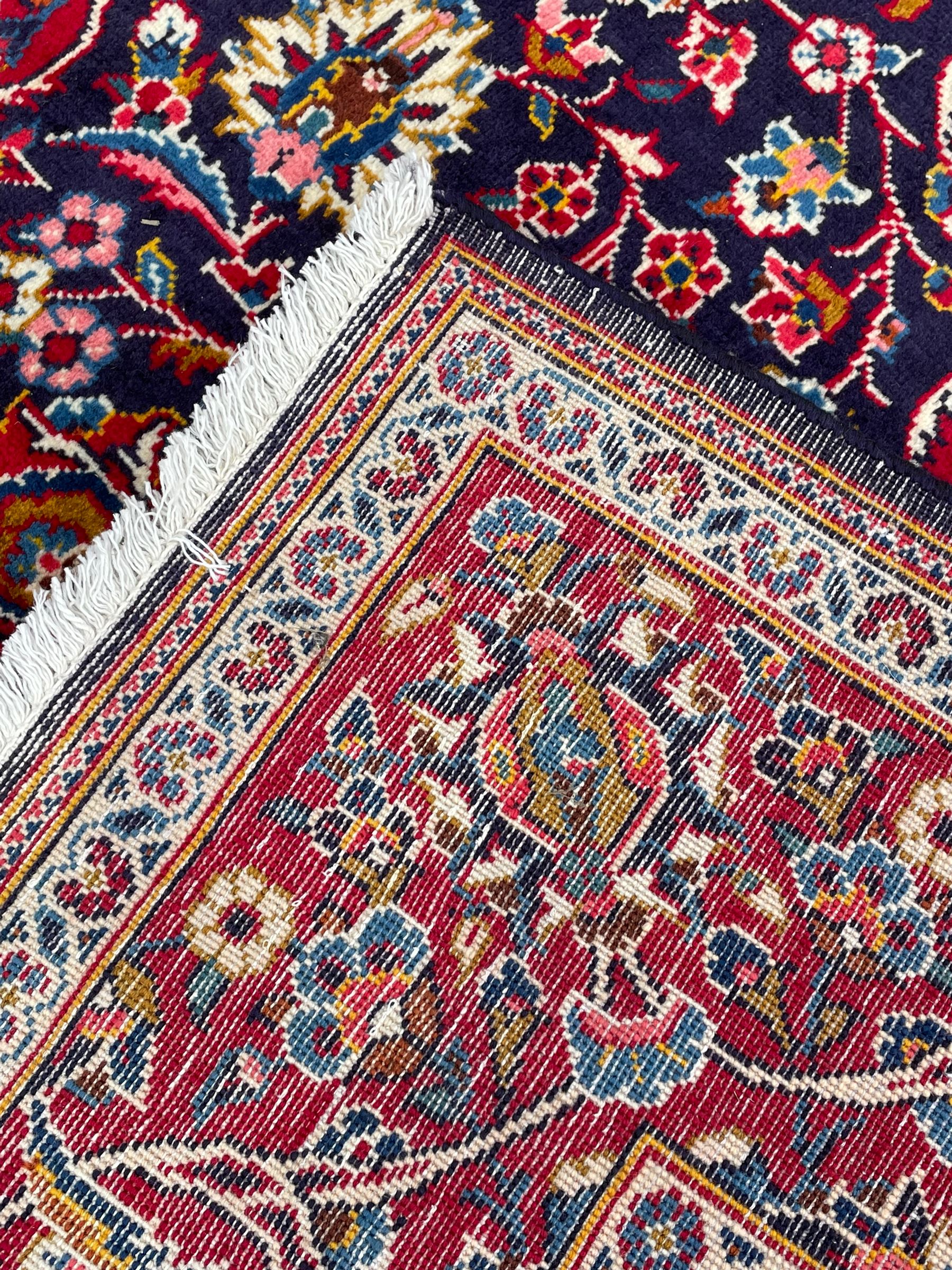 Persian indigo ground rug, the central crimson pole lozenge medallion surrounded by interlacing floral patterns, the main border with repeating plant motifs connected by scrolling branches