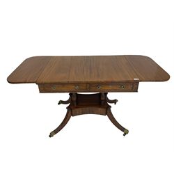 Regency period mahogany drop-leaf sofa table, rectangular top fitted with two cockbeaded drawers with ebony stringing, raised on turned columns united by quadrupod base, the sabre supports terminating in brass cups and castors