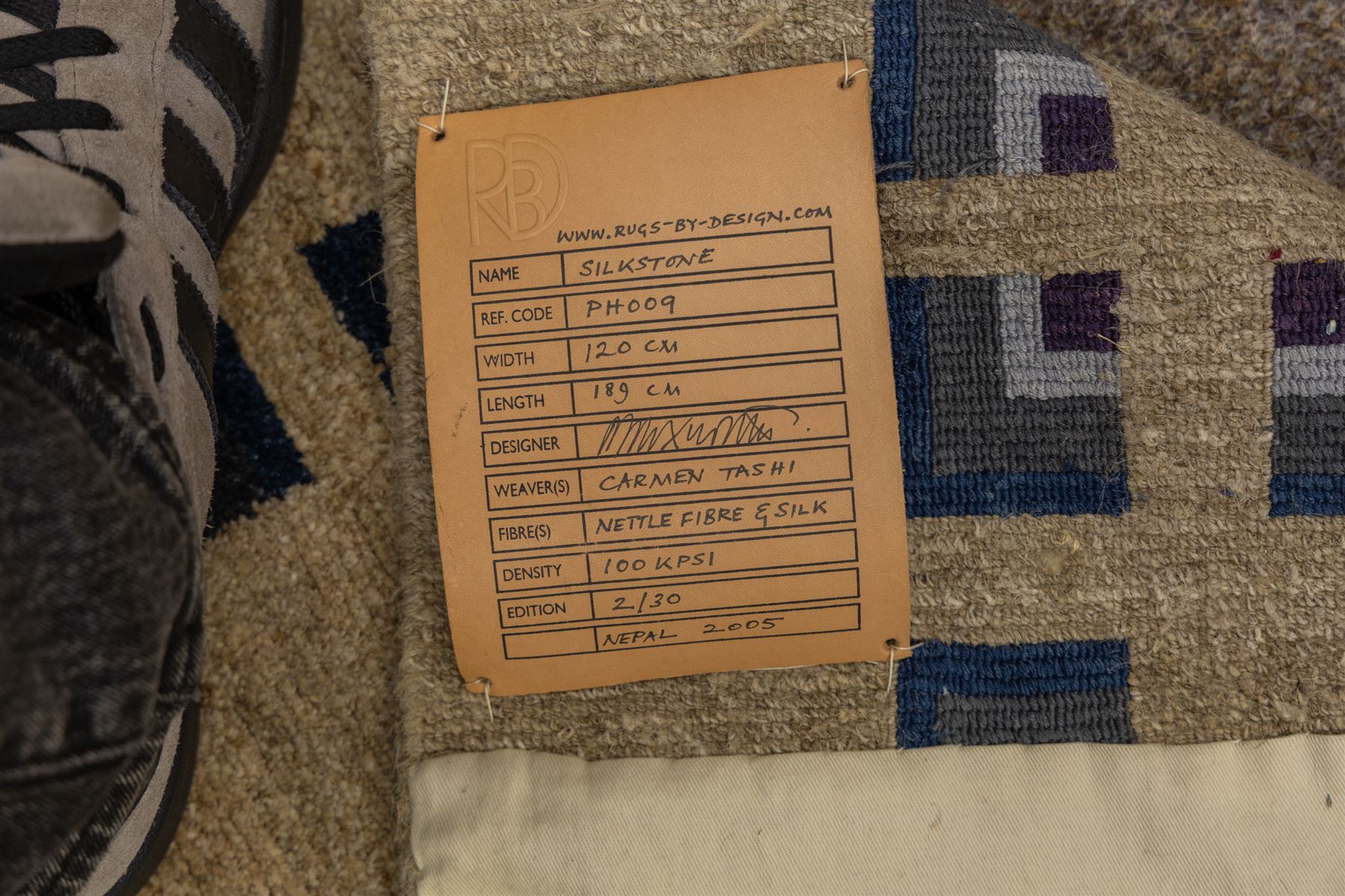 Rugs by Design - ‘Silk Stone’ Nepalese thick pile wool rug, with plain textured camel ground and geometric border detail in blue, grey and dark tones to two sides