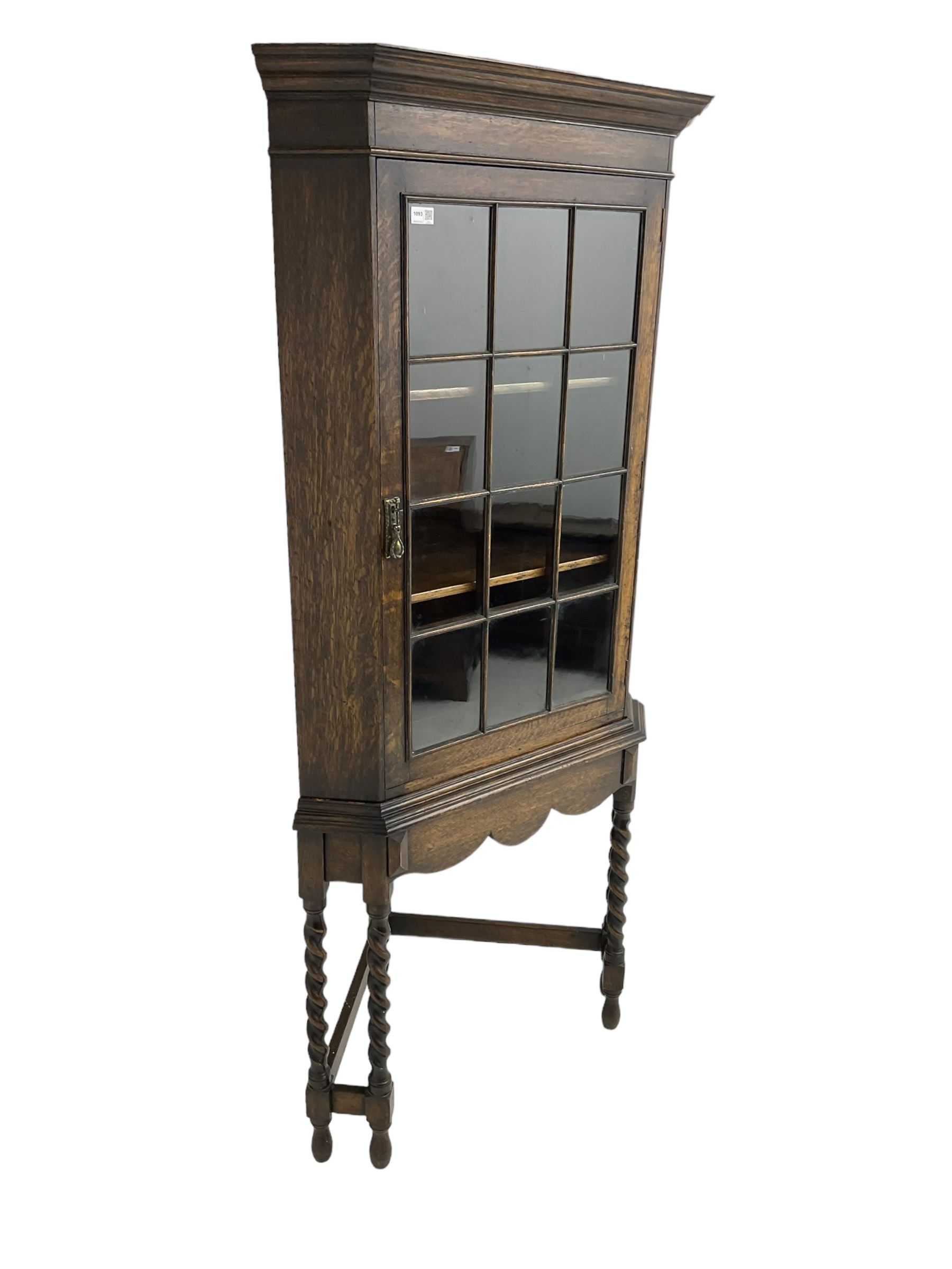 Early to mid-20th century oak corner display cabinet, projecting cornice over astragal glazed door, on spiral turned supports joined by stretchers