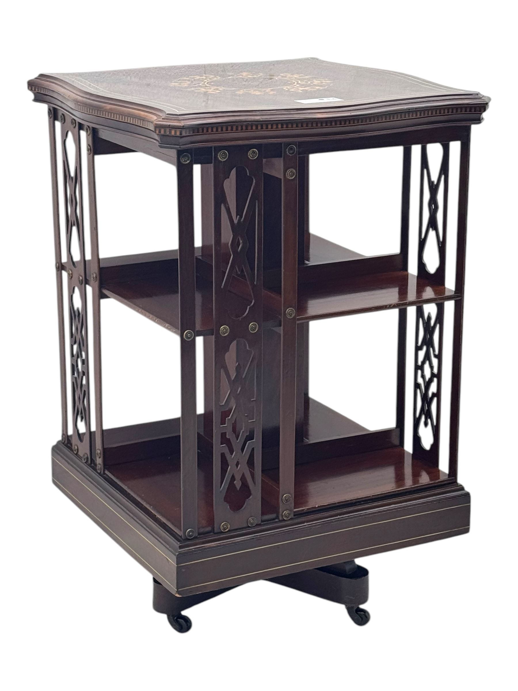 Edwardian inlaid mahogany revolving bookcase, shaped square moulded top with central motif and satinwood band, two tiers with pierced vertical splats, on swivel action base with ceramic castors