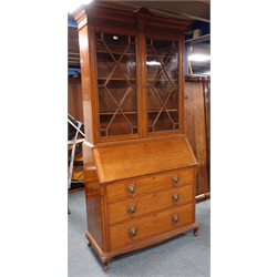  Early 20th century oak bureau bookcase, shell carved projecting cornice, blind fret frieze above two astragal glazed doors, four shelves, fall front enclosing fitted interior, three graduating drawers, W115cm, H234cm, D53cm  
