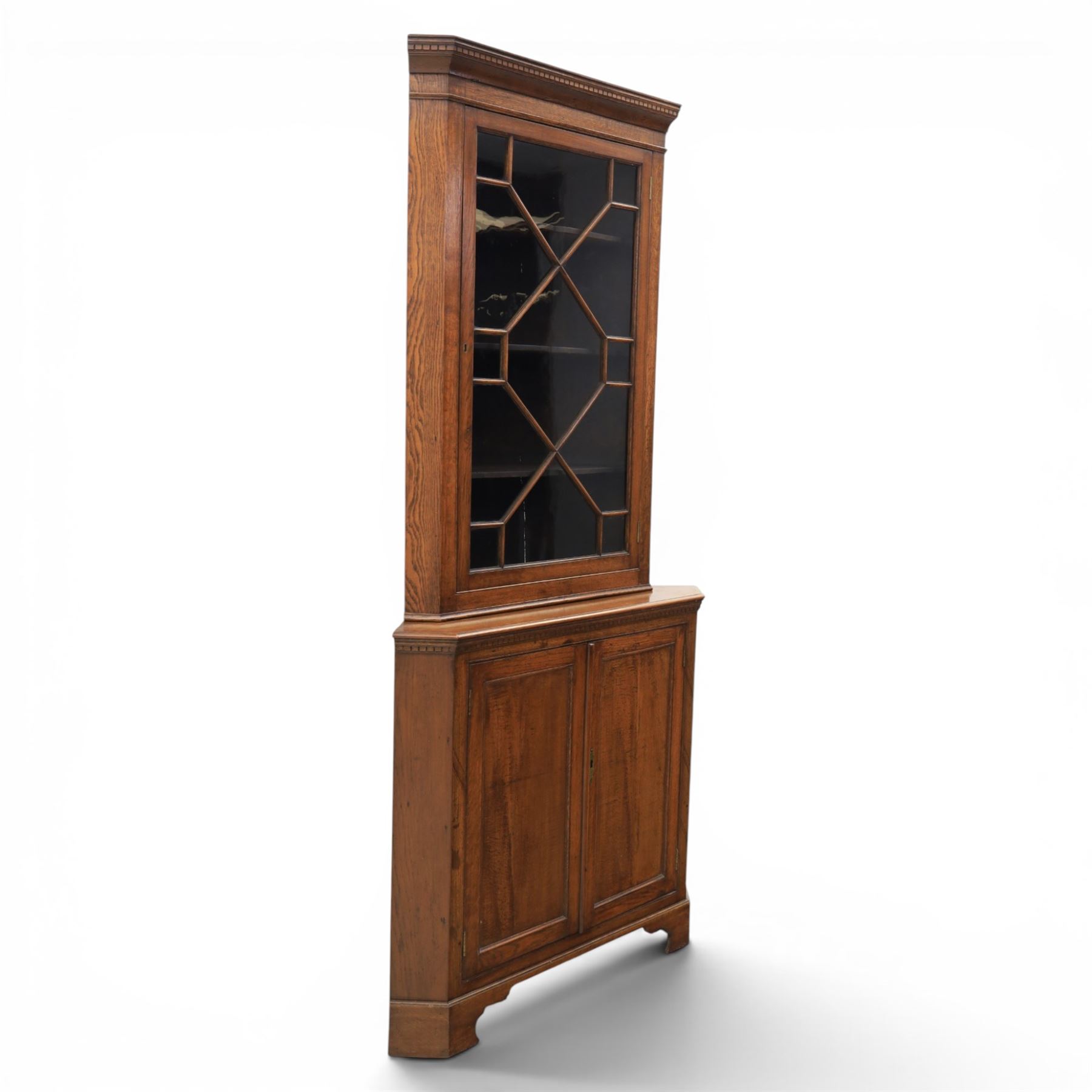19th century oak floor-standing corner display cabinet, dentil cornice above astragal glass, shaped fixed shelves, the lower section with twin cupboard doors, on shaped bracket feet