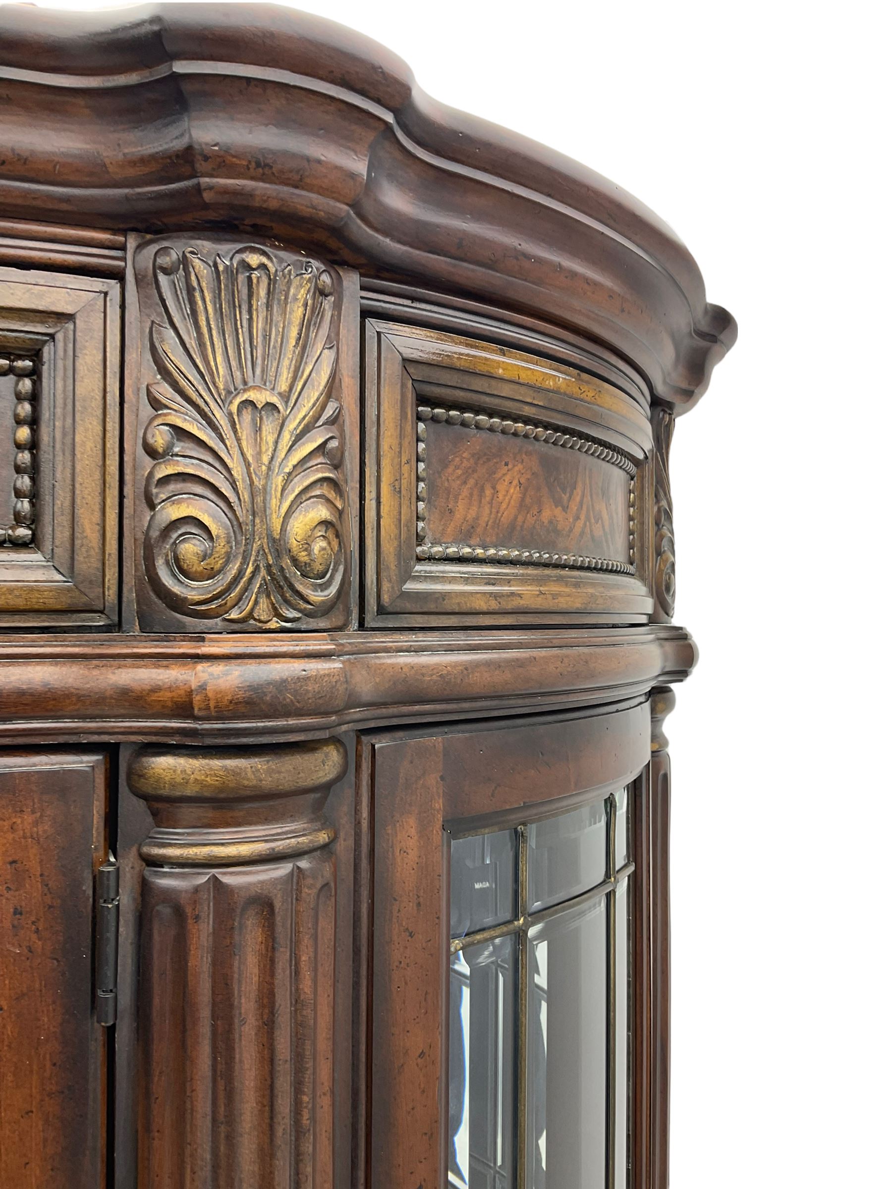  Kevin Charles American walnut demi lune display cabinet with illuminated interior, projecting cornice, two bevel edge glazed doors enclosing two adjustable shelves above single drawer and four cupboard doors with wine rack, carved scrolling supports