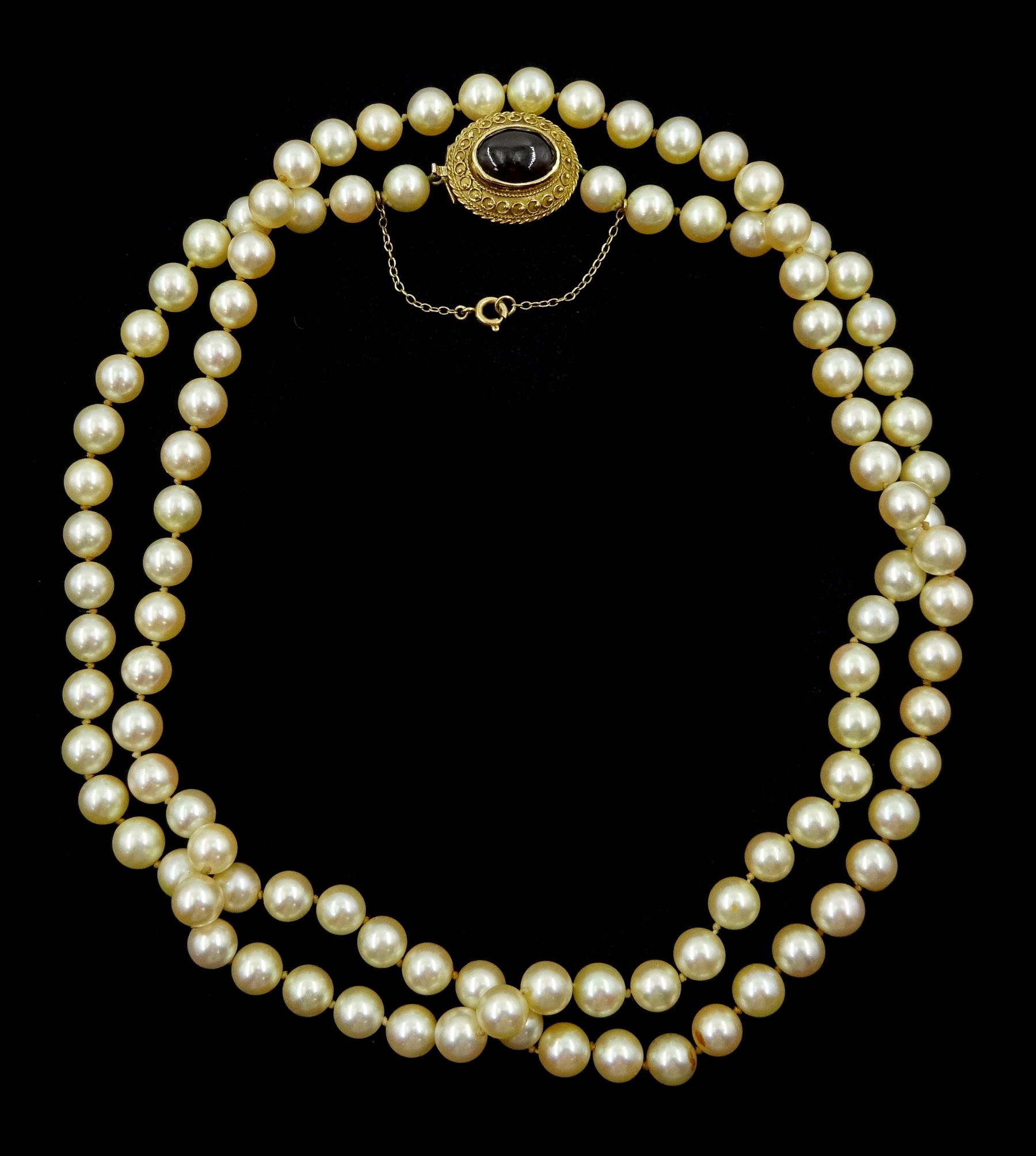 Single strand cultured cream / pink pearl necklace, on a gold cabochon garnet clasp, stamped 9ct