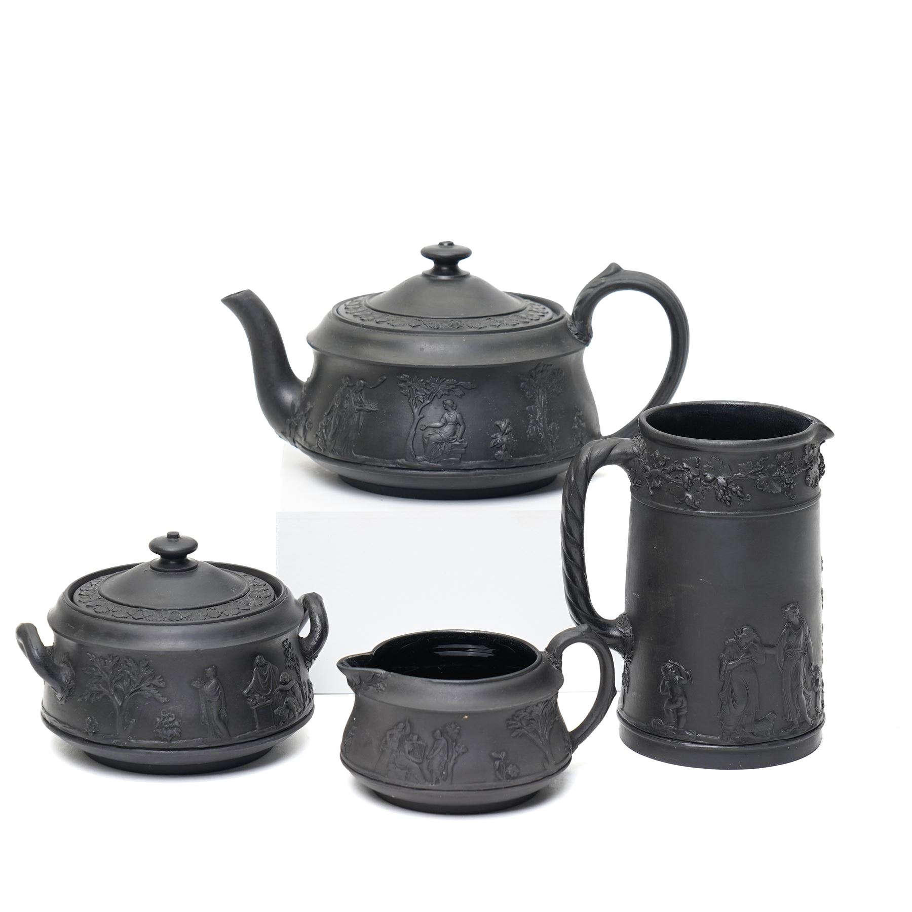 Four pieces of 19th century Wedgwood black basalt ware, c.1875, comprising larger and smaller jug, covered sucrier and teapot, each decorated with classical scenes in high relief, larger jug H13cm