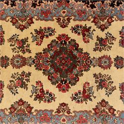 Central Persian Kashan hand-knotted carpet, cream ground, with a central lobbed floral burgundy, rose, and indigo medallion, surrounded by scrolling sprays of carnations and palmettes, with sky blue spandrels decorated with curvilinear vines and stylized blossoms, framed by a repeating terracotta border of palmettes, framed by narrow guard stripes 