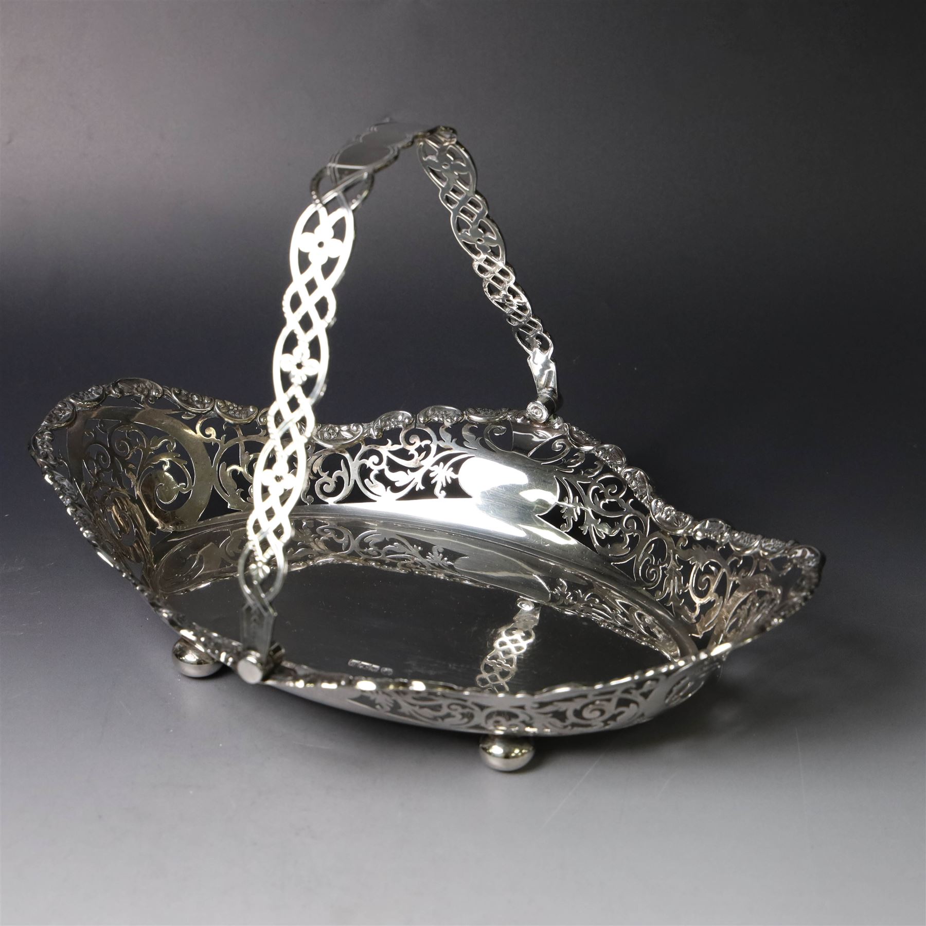 Early 20th century swing handled basket, of oval form with pierced sides and floral C scroll rim, upon four bun feet, hallmarked William Hutton & Sons Ltd, Sheffield 1915, widest point W29cm