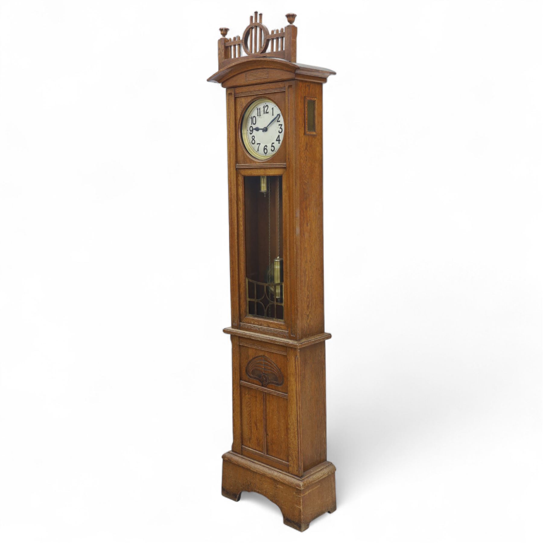 German-Art Deco 8-day longcase clock in an oak case, with a curved top and open fence work pediment, with reeded decoration and a fully glazed case door with a rectangular brass open work panel, on a tall rectangular plinth with a period  carved motif, circular slivered dial with Arabic numerals and spade hands, two train HAC (Hamburg and American Clock Company) weight driven movement, sounding the hours and half-hours on a coiled gong, with weights and pendulum.   