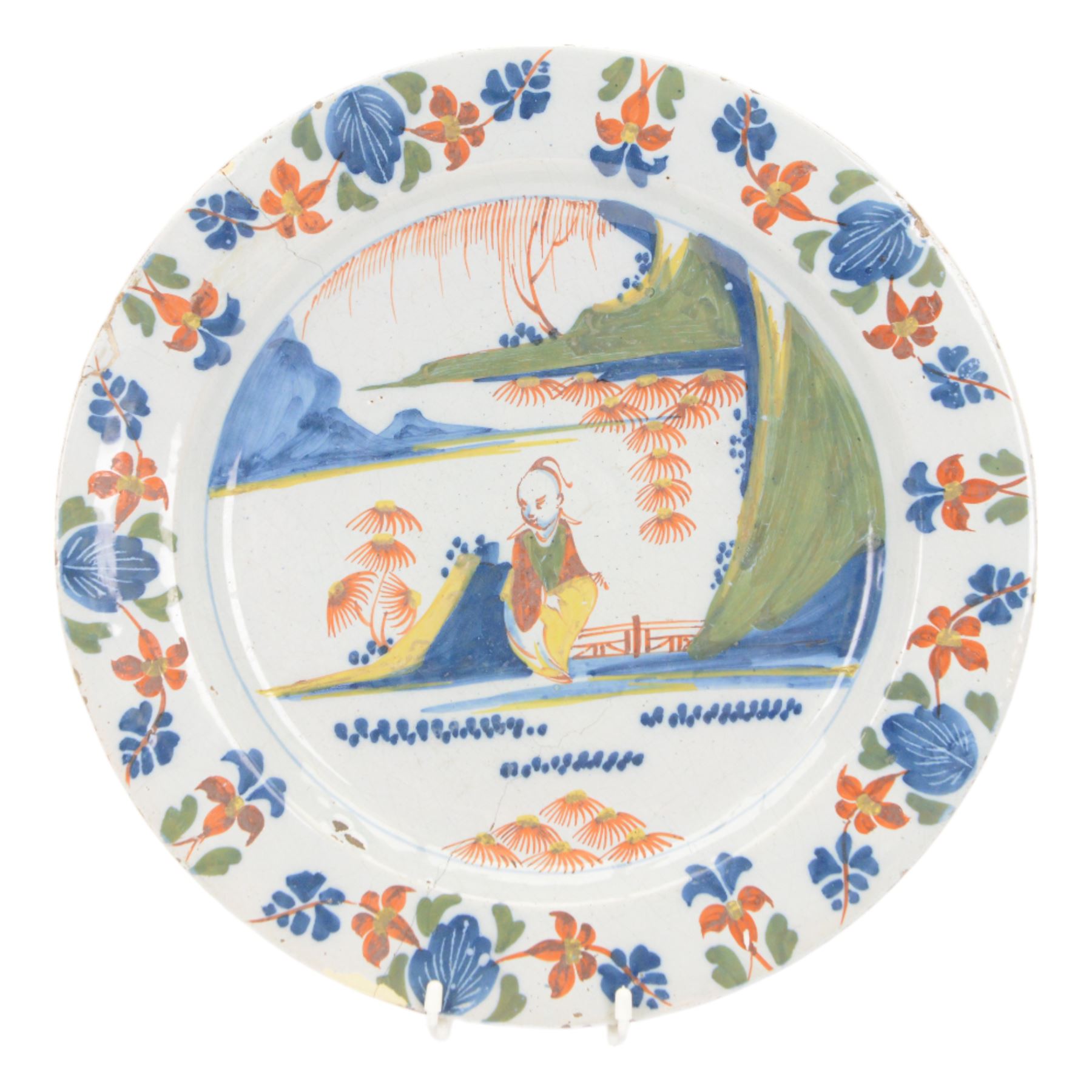 Mid 18th century Lambeth Delft plate, probably from the Abigail Griffith factory, circa 1750, painted in polychrome enamels with a figure seated in a landscape, within a garlanded border of flowers to rim, D34cm, together with a Liverpool Delft plate, circa 1760, painted in blue with a boathouse surrounded by trees by a river, within diaper and cell borders, D37cm