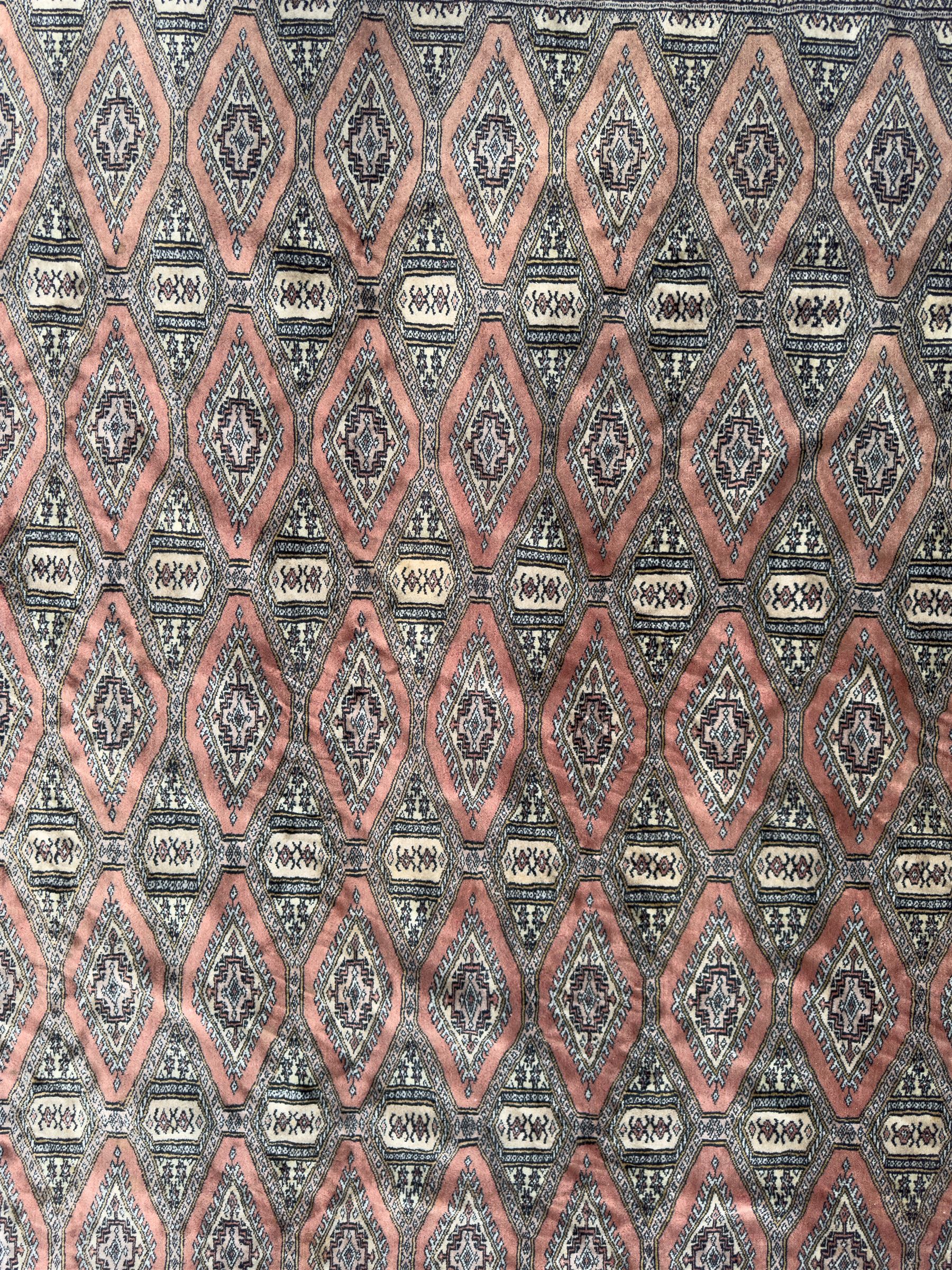 Large Persian Bokhara wool rug, the field decorated with repeating gul motifs in lozenge medallions across a dark ground, enclosed by multiple geometric borders in indigo, ivory and terracotta, from the region of Baluchistan