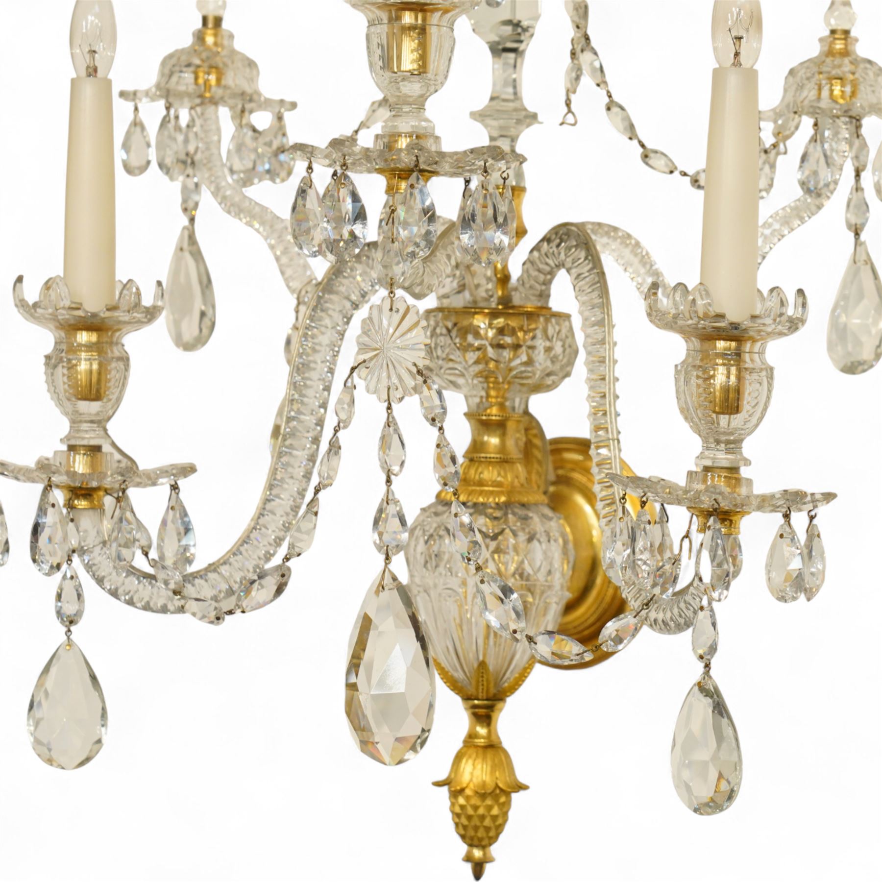 Pair of George III ormolu and cut-glass wall-lights, each with a tall central urn-shaped finial above a series of faceted glass spires and scrolled branches, the ormolu-mounted nozzles and drip pans hung with festoons of cut-glass drops and pear-shaped pendants, the lower section centred by a pineapple finial, wired for electricity