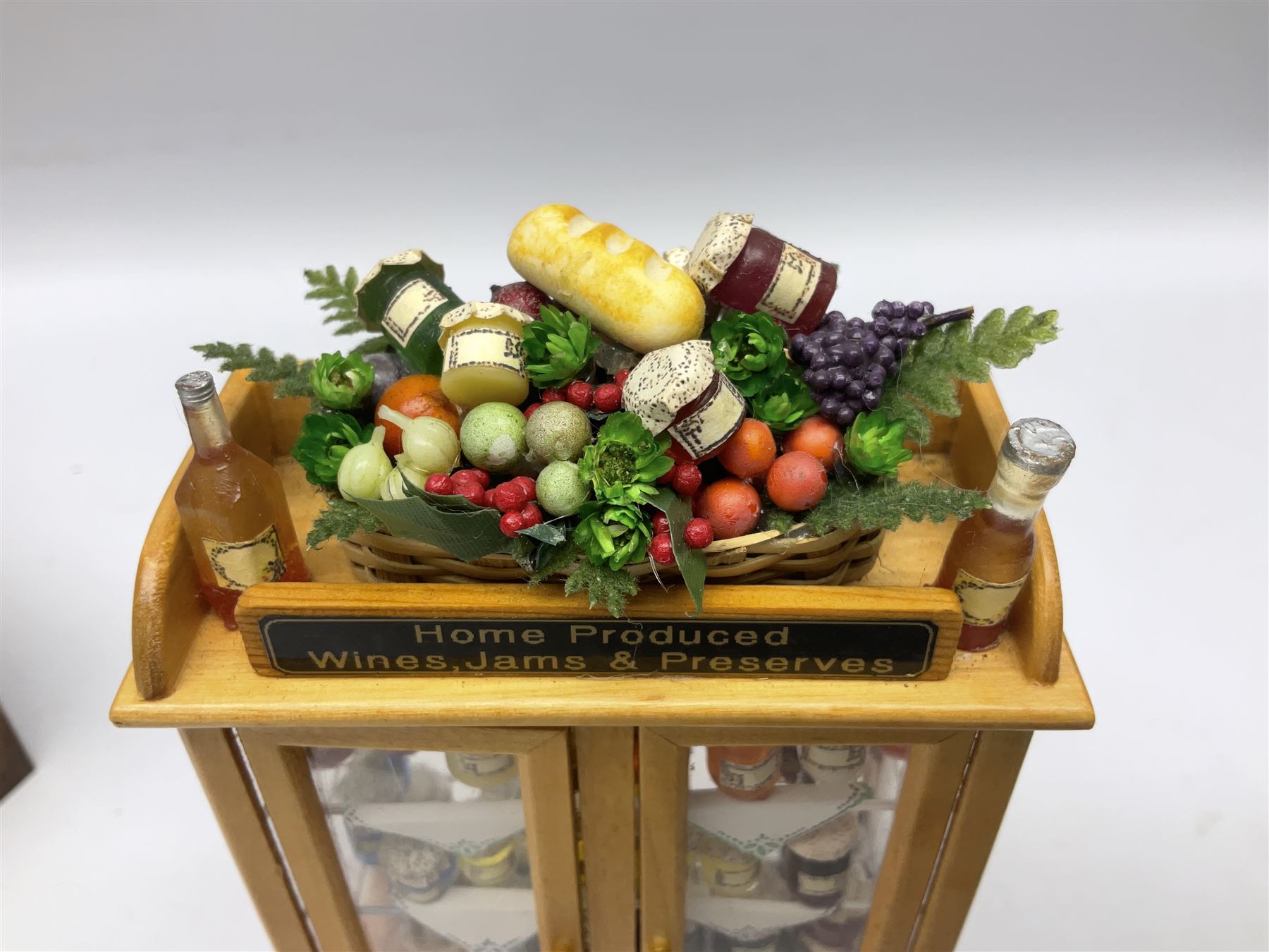 Collection of miniature dolls house grocery shop furniture and produce, comprising glazed corner counter with brass style cash register, shelved preserves unit, pies, cheese board and trays of meats, pair of white cheese counters, biscuit display with six tins, glazed preserves cabinet, pair of shop chairs and four further cheese boards complete with grapes and label flags