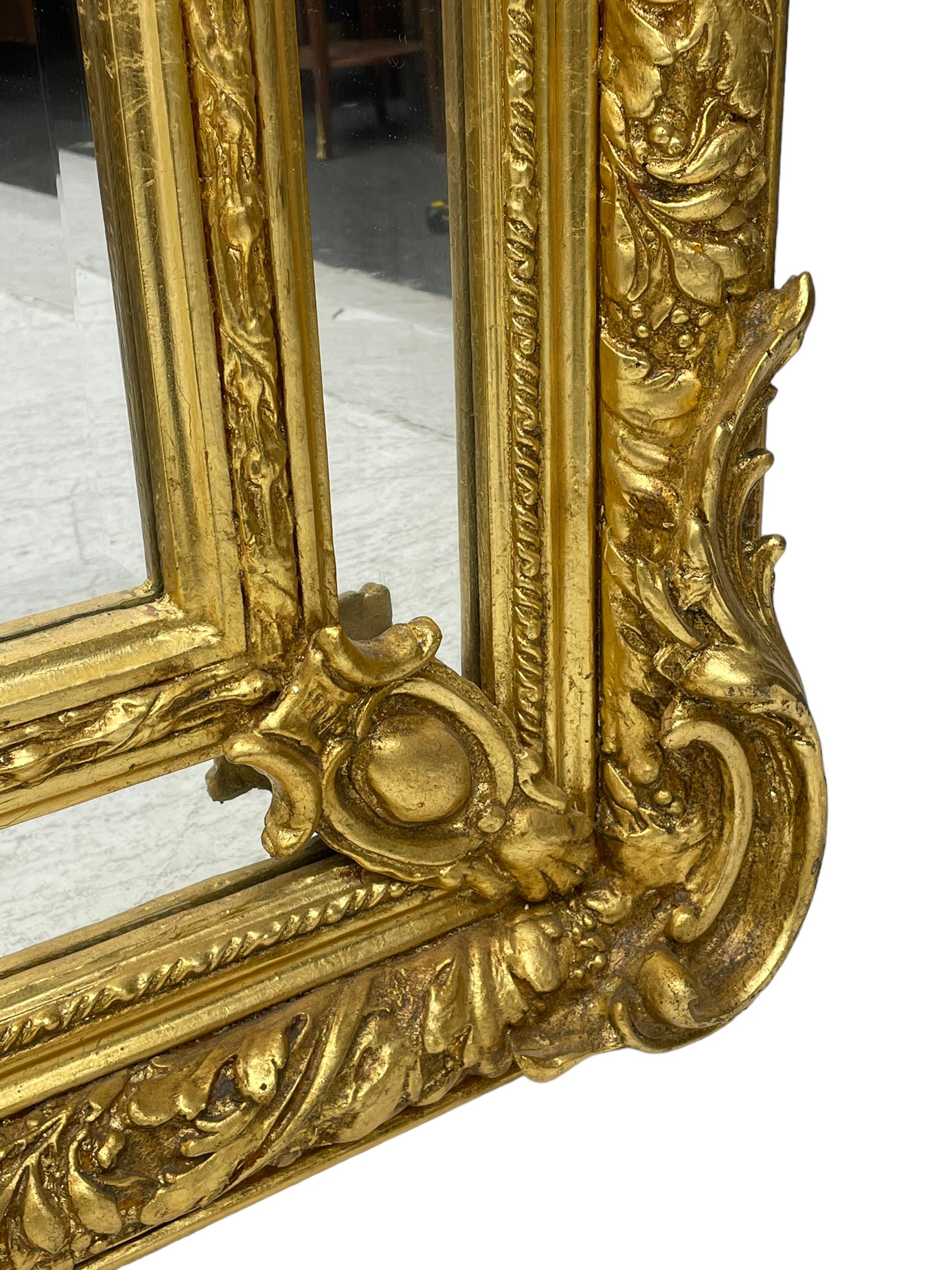 Large Italian Baroque design gilt wall mirror, the shell pediment over circular panel depicting classical female flute player with dancing putto within a tree landscape, the stepped arched upper frame surmounted by musical instrument playing putto and trailing flower heads, central bevelled mirror plate surrounded by plain segmented mirror plates, acanthus leaf moulded outer frame and foliate moulded inner slip
