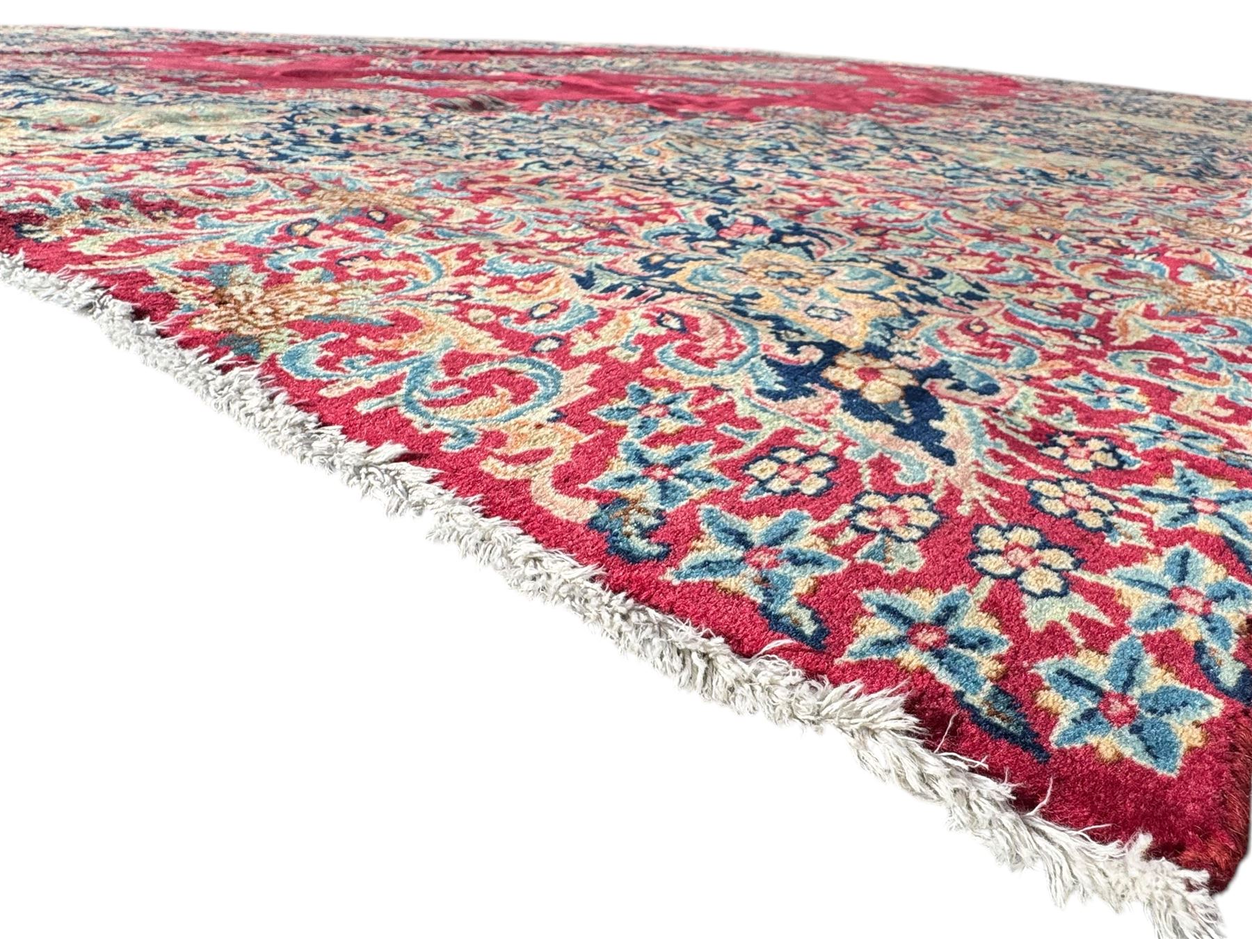 Persian Kirman carpet, the bold ruby field hosting a multi-lobed central medallion, embellished with scrolling vines and floral sprays, edged by layered borders and trimmed with short fringe