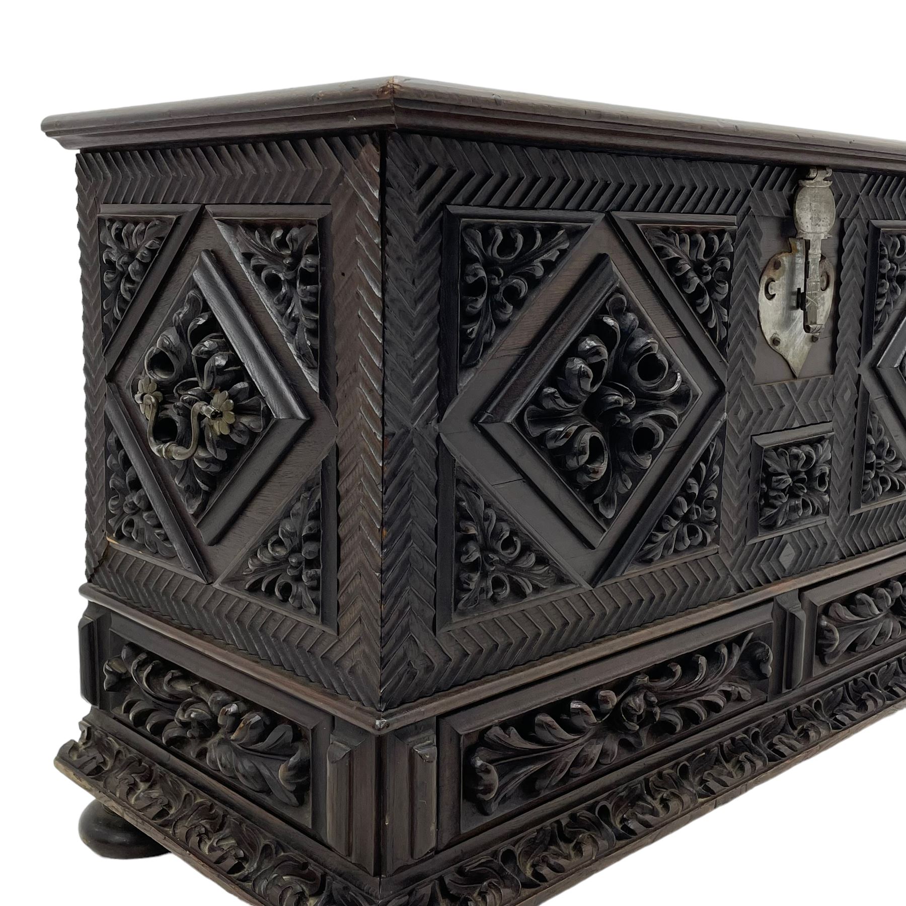 Early 20th century carved hardwood kist or mule chest of small proportions, moulded rectangular hinged lid over foliage carved geometric lozenge panels, the frame carved with chevron banding, fitted with two drawers, the drawer fronts carved with extending leaf motifs over a foliage carved lower moulding, on turned feet