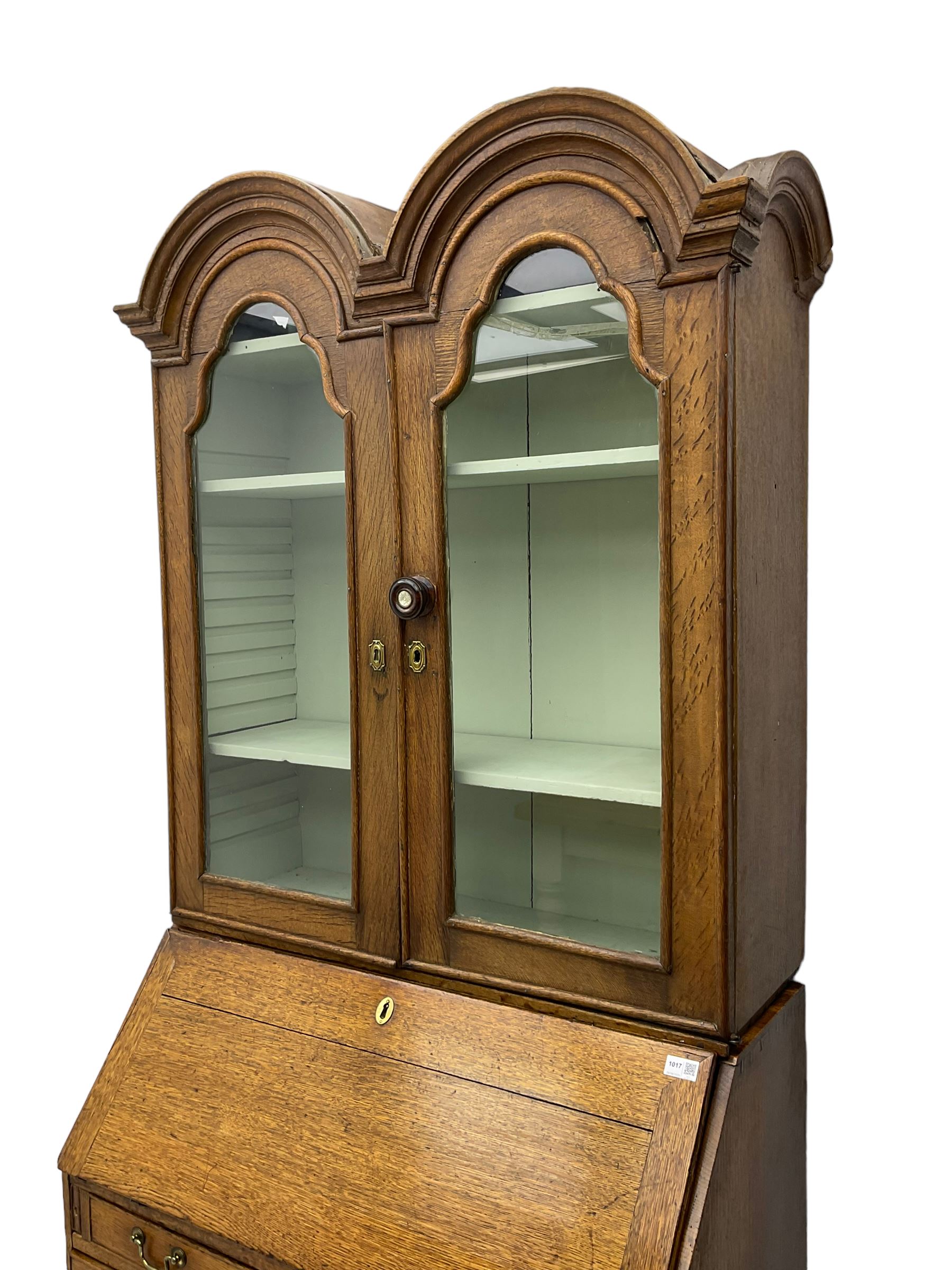George III oak bookcase on bureau, the double arched top enclosed by two shaped glazed doors, fall-front concealing fitted interior, over four graduating cock-beaded drawers, on bracket feet