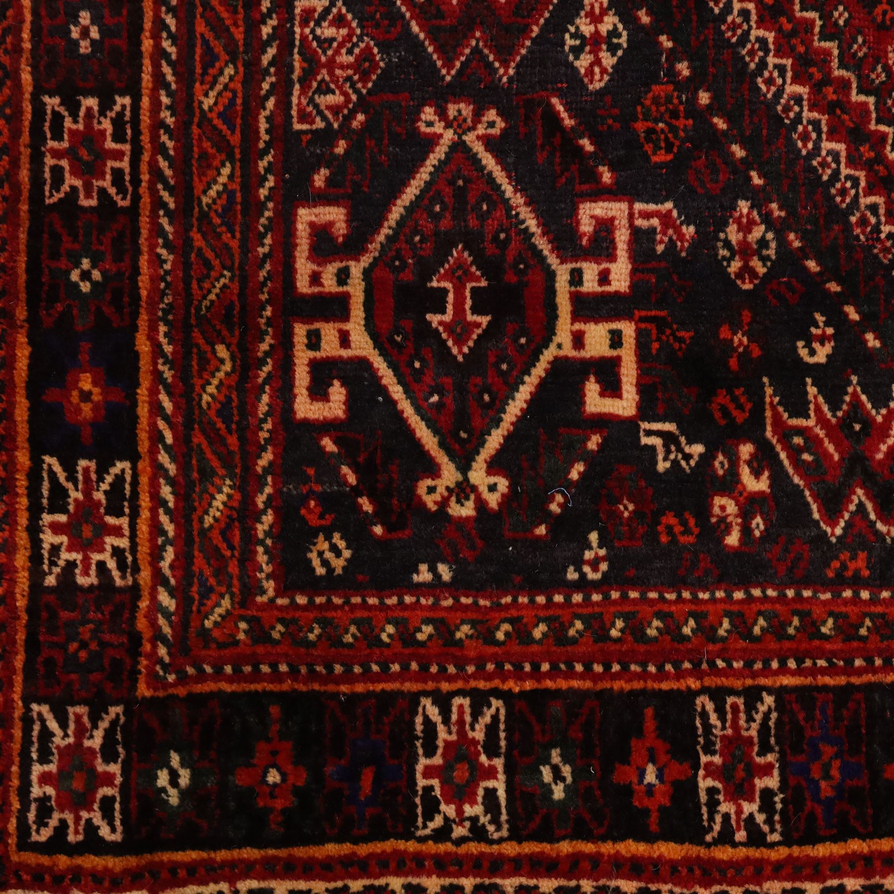 South West Persian Qashqai hand-knotted rug, madder red field with a large stepped diamond medallion with scattered geometric devices and indigo spandrels filled with geometric motifs, framed by multiple narrow guard borders and broad main border, wool fringe ends 