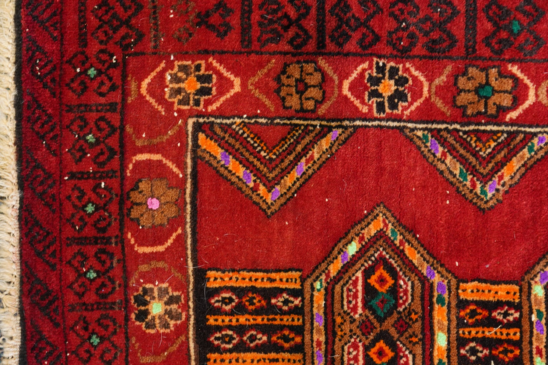 Persian Baluchi crimson ground rug, decorated with three columns of geomtric motifs
