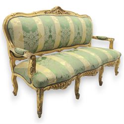 20th century French Louis XV style giltwood salon sofa, with shaped and moulded serpentine cresting rail carved with central scroll motif, padded back and seat upholstered in green and gold striped damask fabric, scroll carved open arms with padded rests, shaped apron carved with rocaille and foliate motifs, raised upon cabriole legs