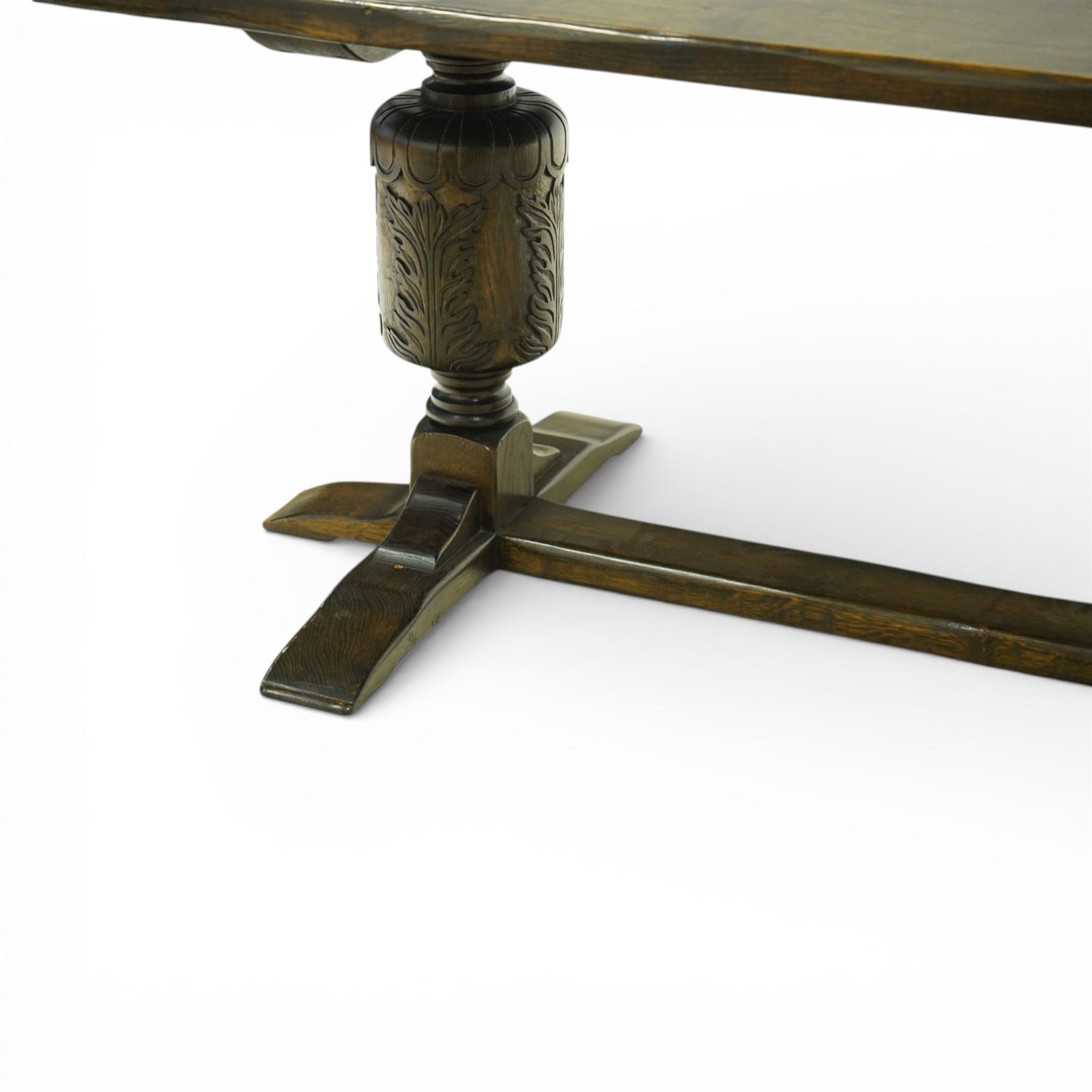 20th century oak refectory style dining table and eight chairs (6 + 2), rectangular top on two large carved baluster pedestal supports with leaf decoration, on splayed trestle bases joined by a stretcher, with eight matching oak dining chairs, each with Yorkshire rose carved cresting rail, panel back and solid seat, raised on turned supports united by stretchers