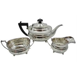 Early 20th century silver three piece tea service, comprising teapot, milk jug and twin handled sucrier, each of oval form with engraved monogram to body, oblique gadrooned rim, scroll capped handles and raised upon four ball feet, the teapot with ebonised handle and finial, hallmarked Martin Hall & Co Ltd, Birmingham 1919, approximate gross weight 30.57 ozt (951 grams)
