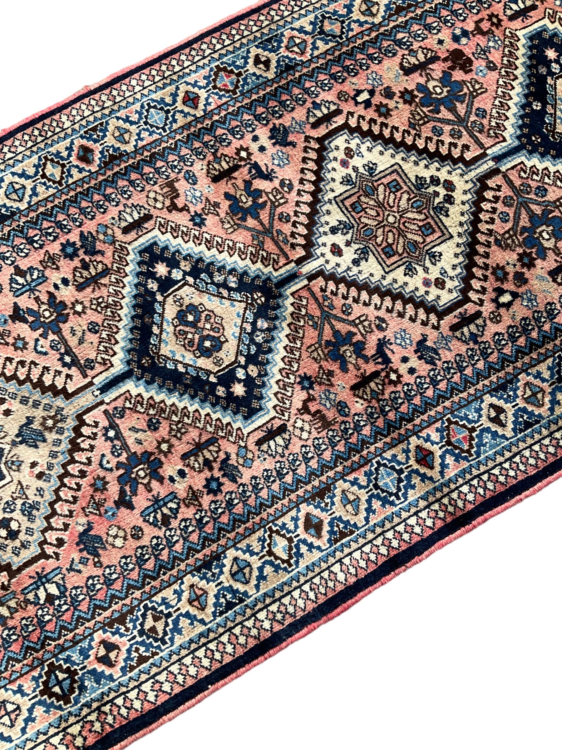 Persian Yalameh coral ground runner rug, the field decorated with seven hooked lozenge medallions surrounded by stylised plant motifs, the indigo spandrels decorated with similar patterns, guarded border with repeating diamond lozenges
